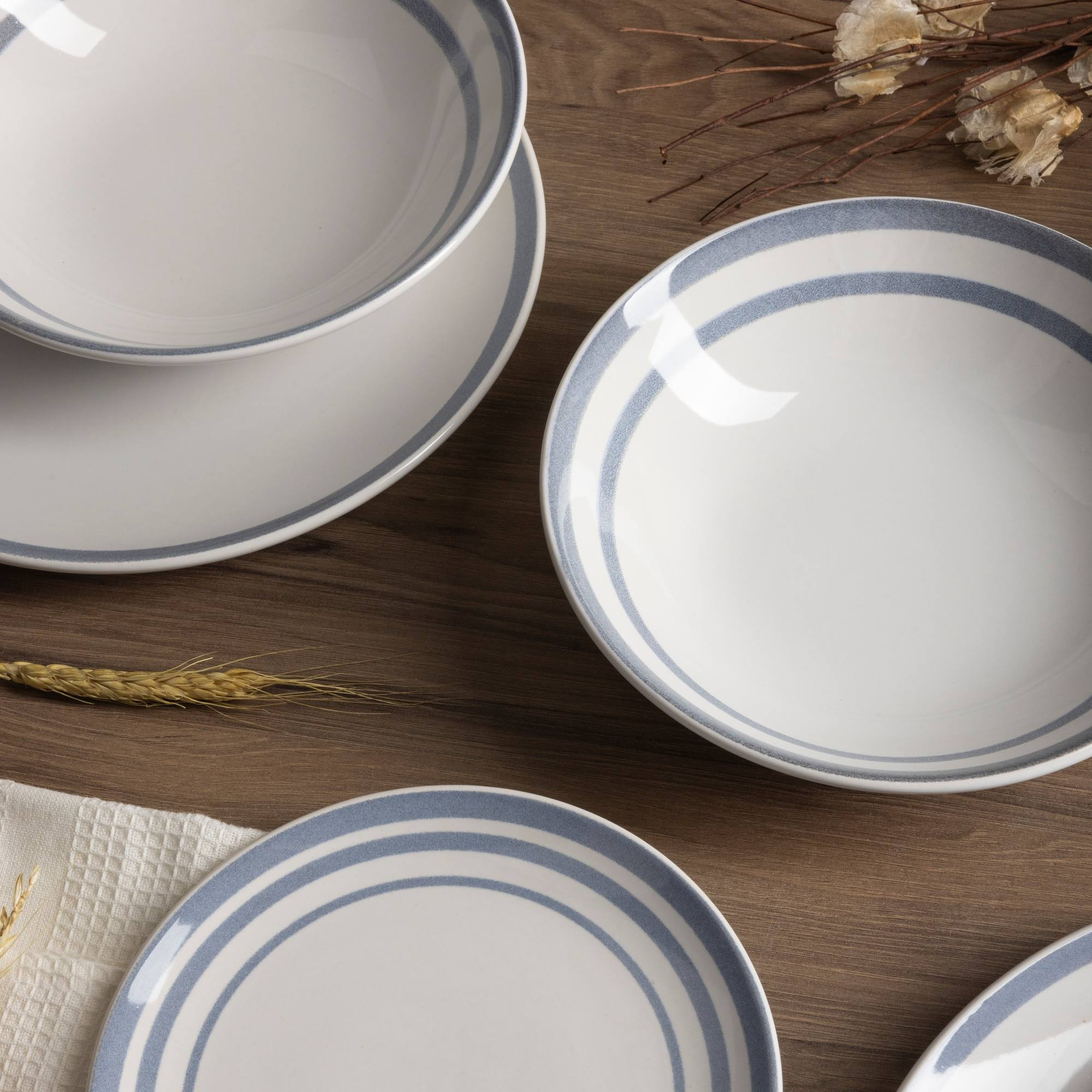 Platos y cuencos blancos con rayas azules sobre mesa de madera.