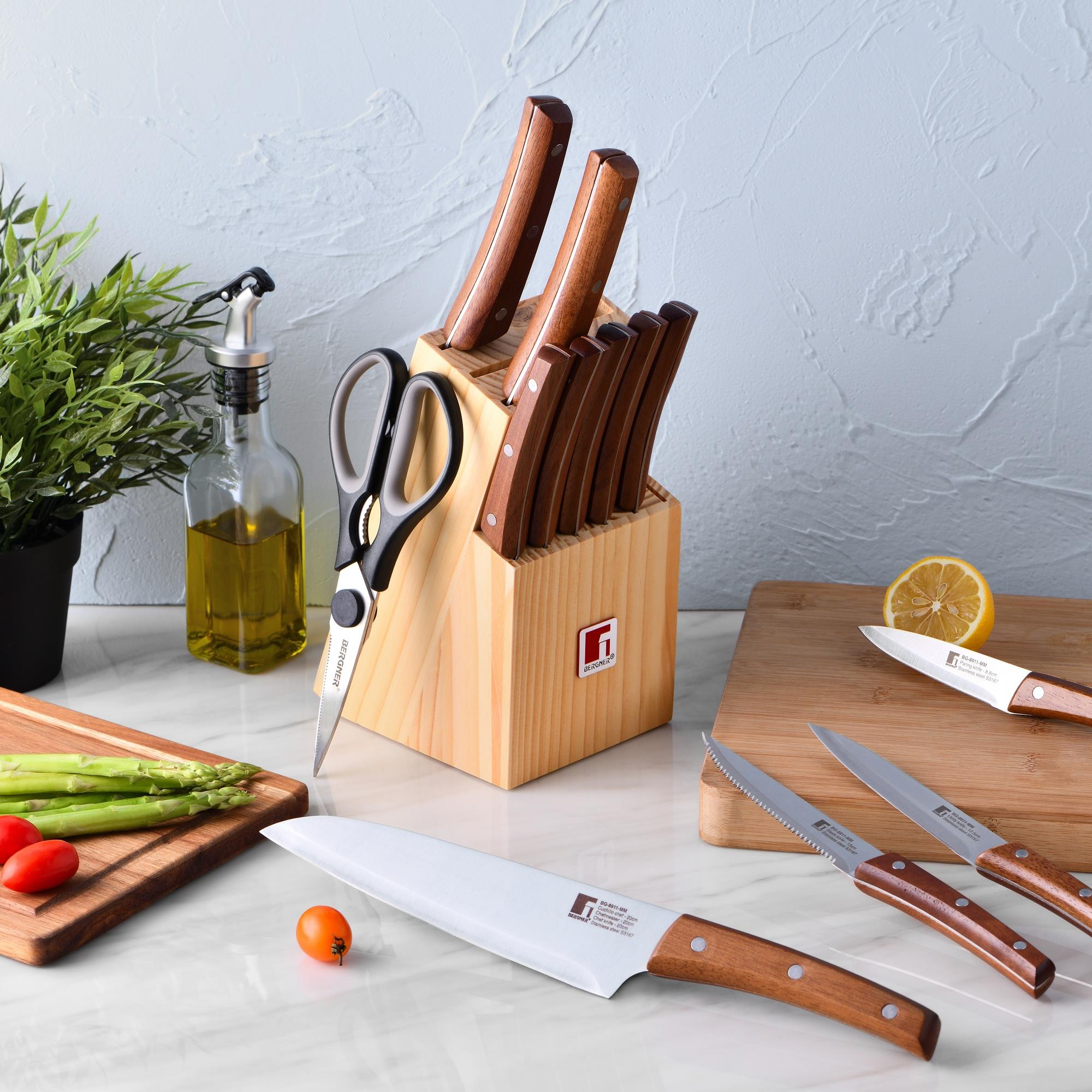 Un bloque de cuchillos de madera con cuchillos, tijeras, botella de aceite, espárragos y tomates.