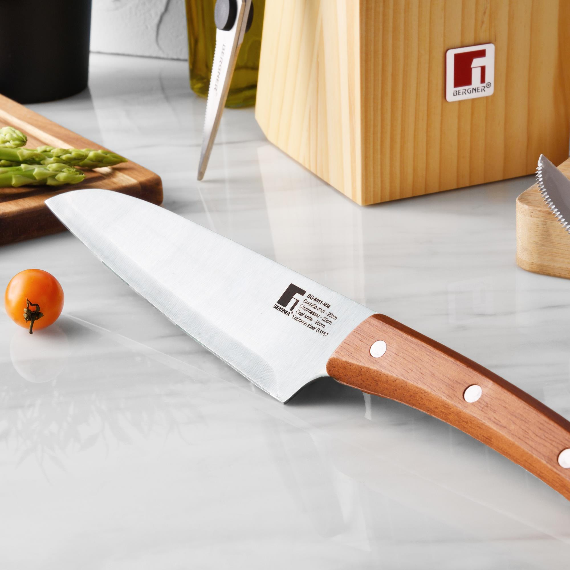 Un cuchillo de chef con mango de madera yace sobre una encimera de mármol junto a espárragos y un tomate.