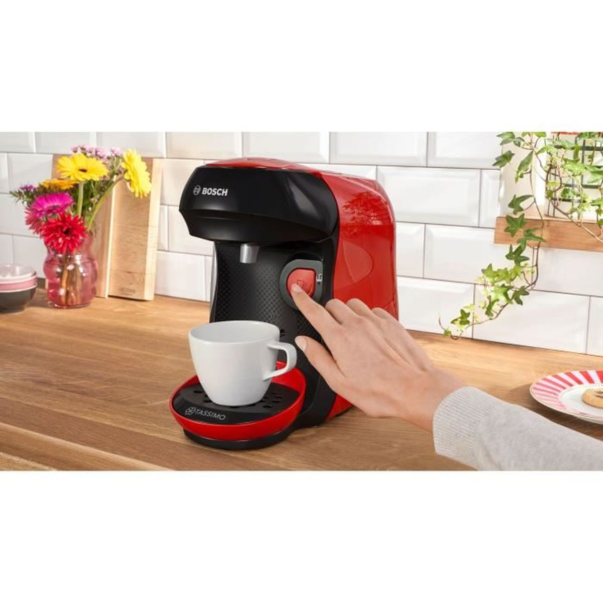 Una mano preme il pulsante rosso su una macchina da caffè Bosch rossa con una tazza bianca.