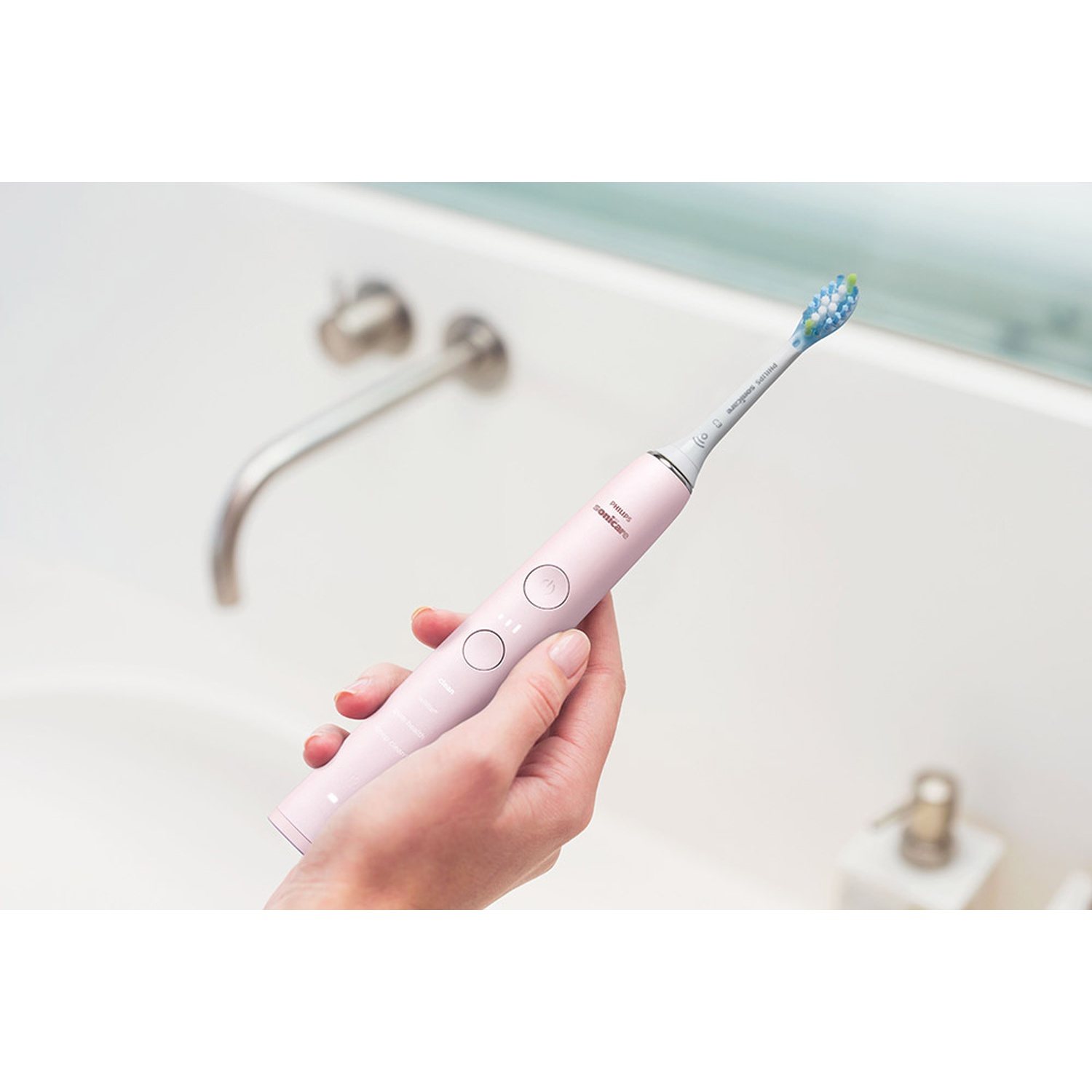 Una mano sostiene un cepillo de dientes eléctrico rosa sobre un lavabo.