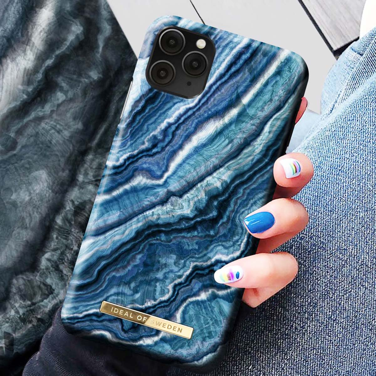 Una mano tiene un telefono con cover effetto marmo blu. Unghie blu.