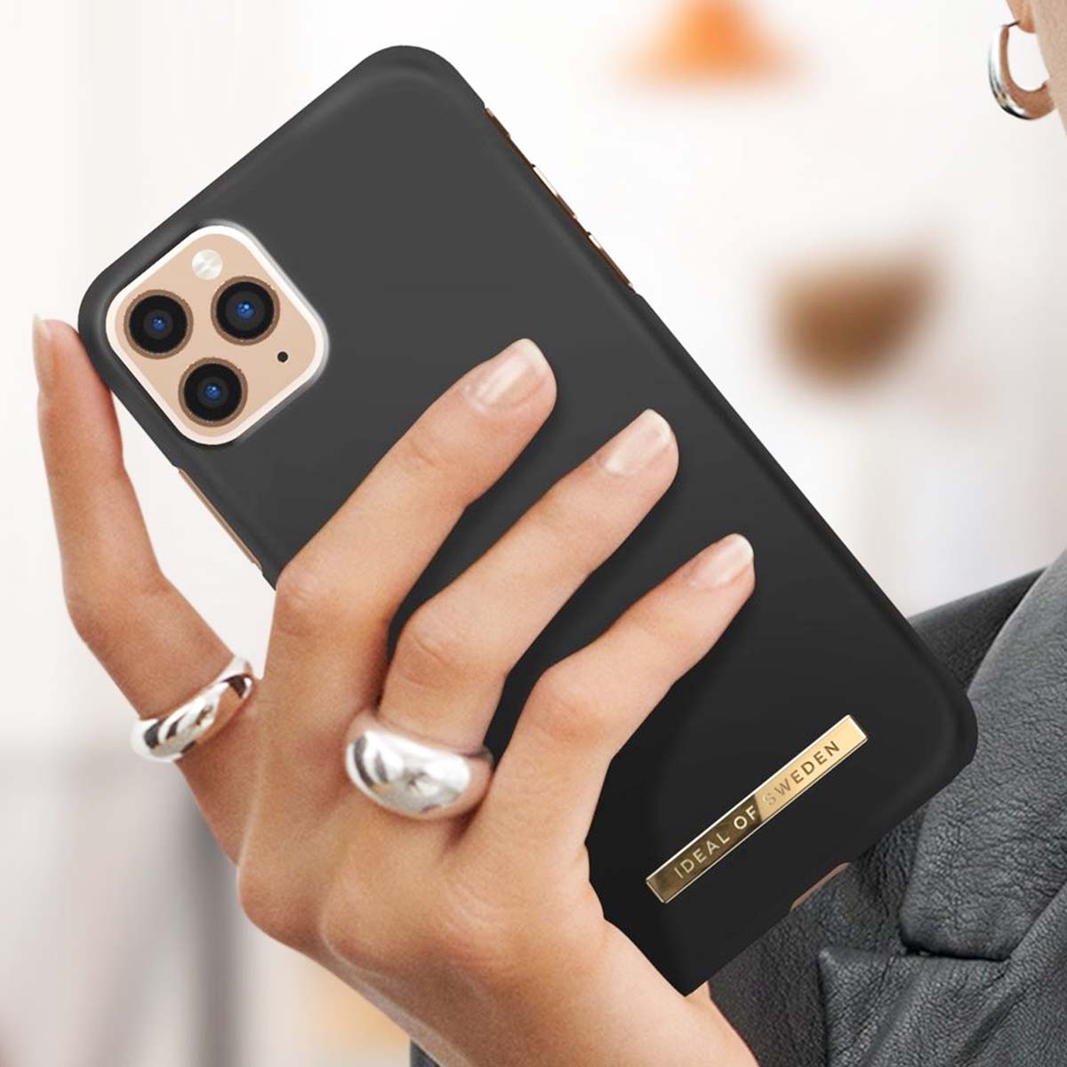 Custodia nera per telefono con tre fotocamere, tenuta da una mano con anelli.