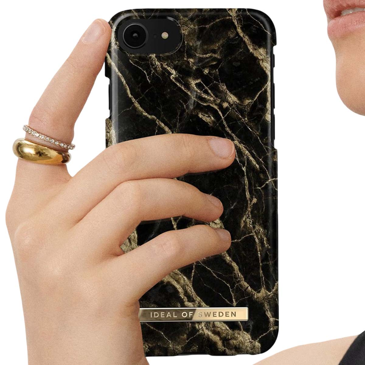 Una mano con anelli tiene una custodia per telefono in marmo nero con scritte dorate.
