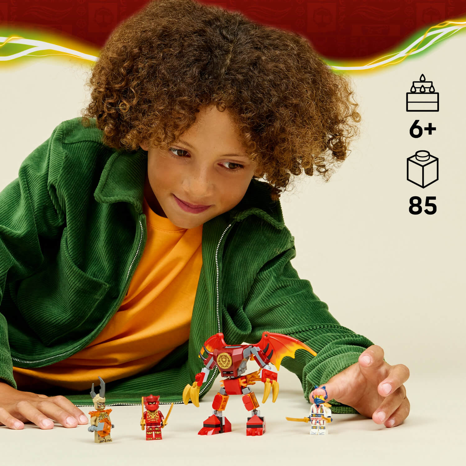 Yeşil ceketli bir çocuk, LEGO figürleri ve kırmızı robot ejderhayla oynuyor.