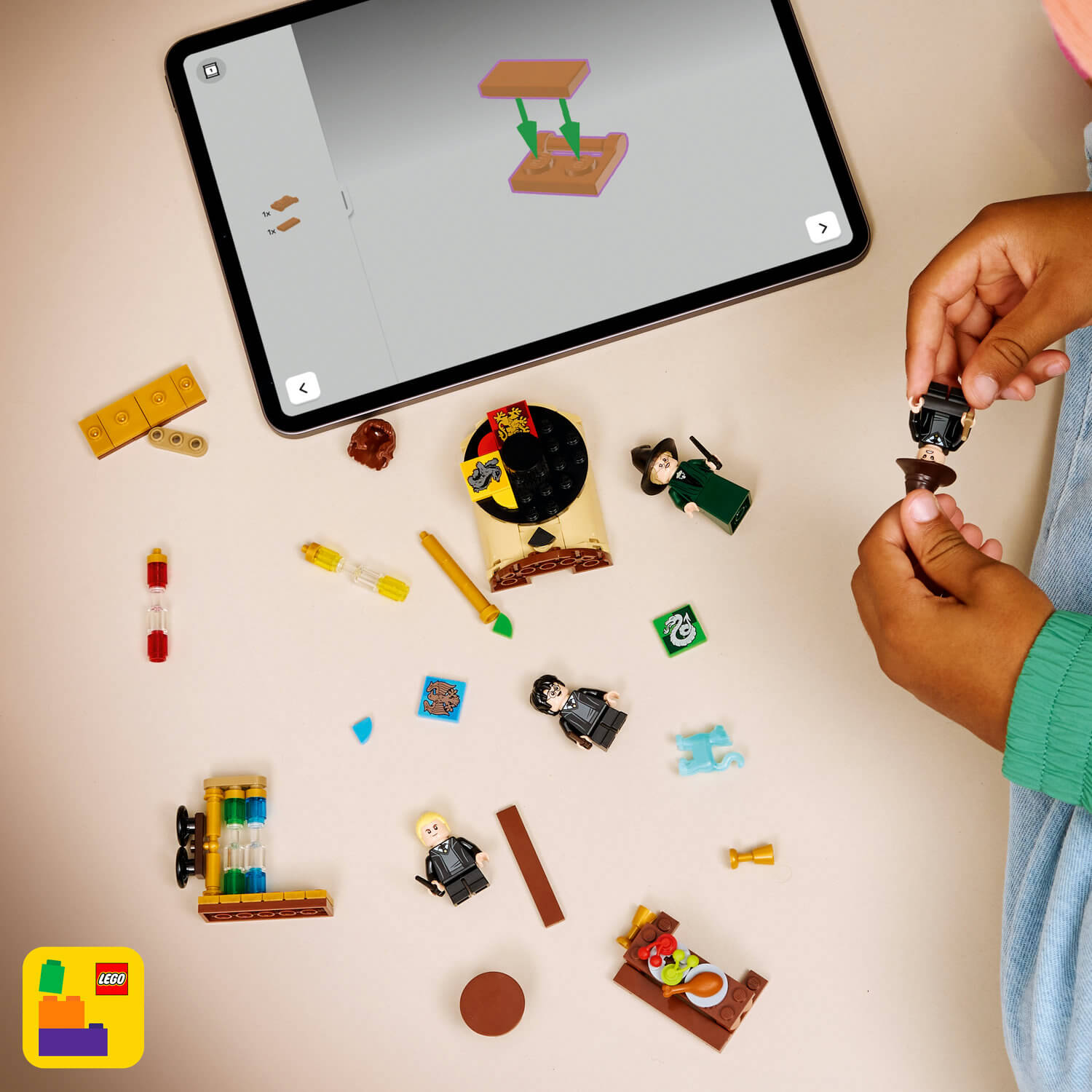 Masa üzerinde LEGO parçaları ve figürleri, uygulama yapım talimatlarını gösteriyor.