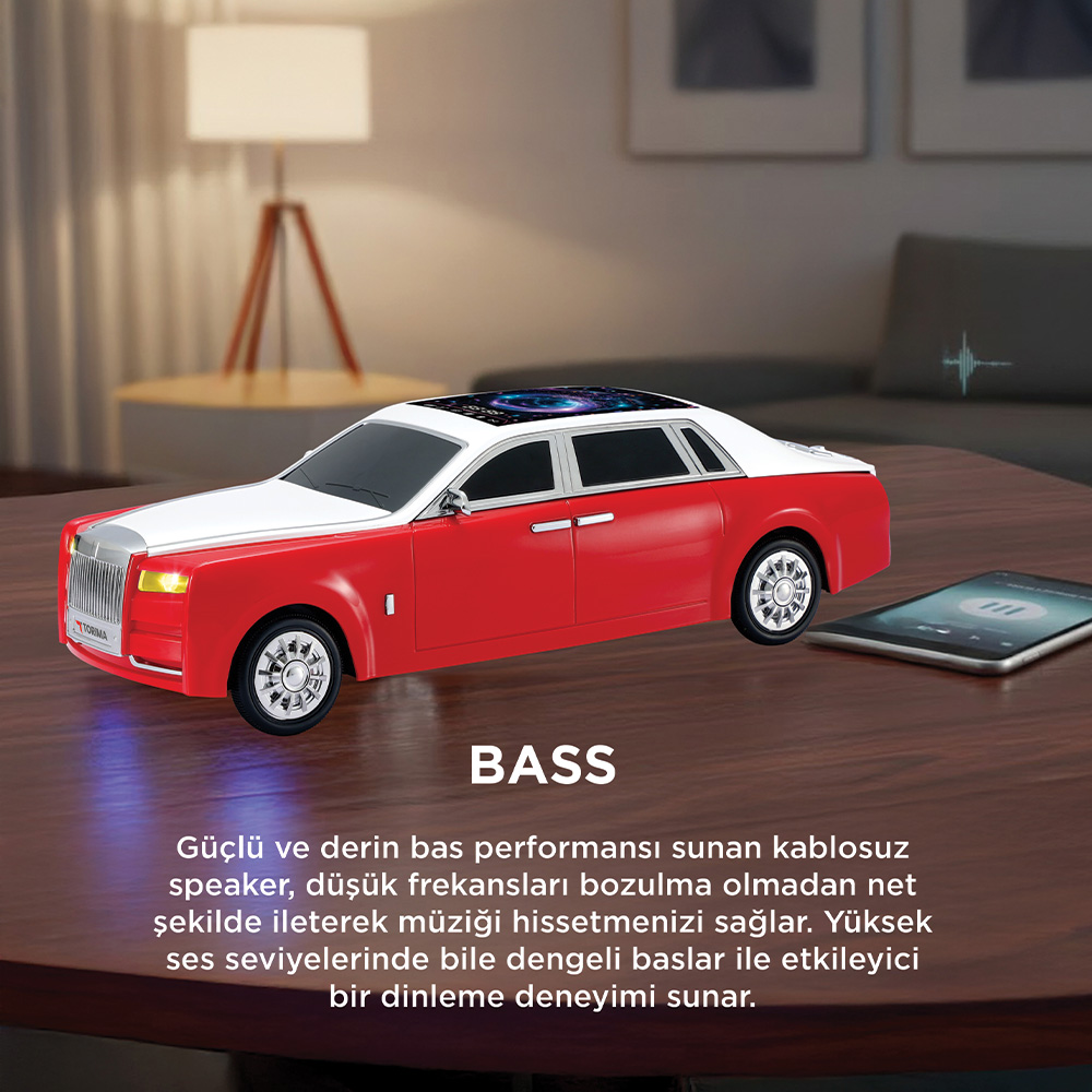 Ahşap masa üzerinde kırmızı ve beyaz araba şeklinde hoparlör, akıllı telefon yanında.