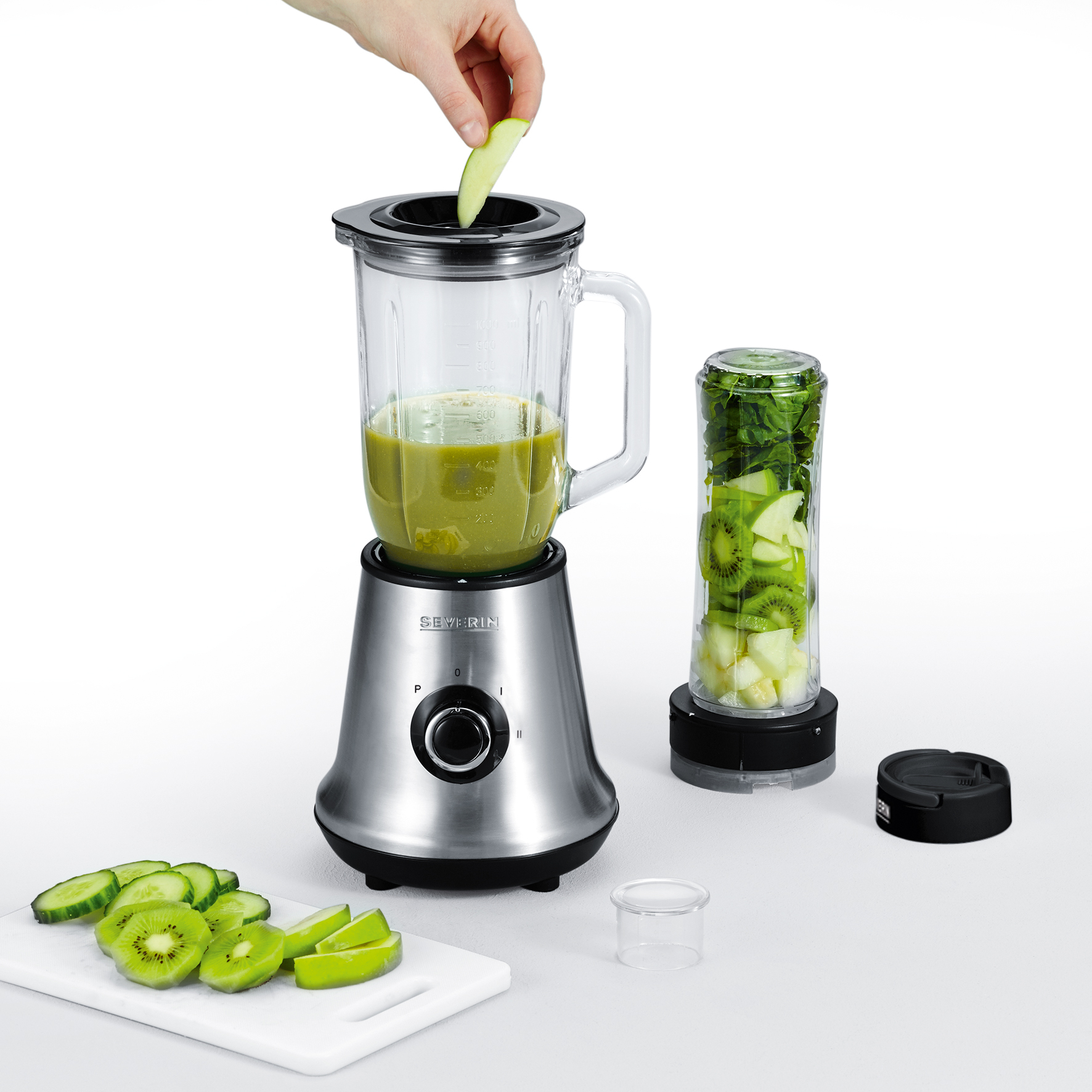 Person gibt Apfelstücke in Mixer mit grüner Flüssigkeit. Obst liegt daneben.