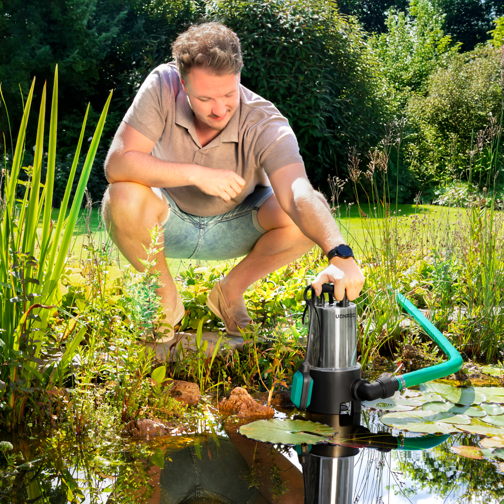 Man hurkt bij vijver, houdt dompelpomp met groene slang vast.