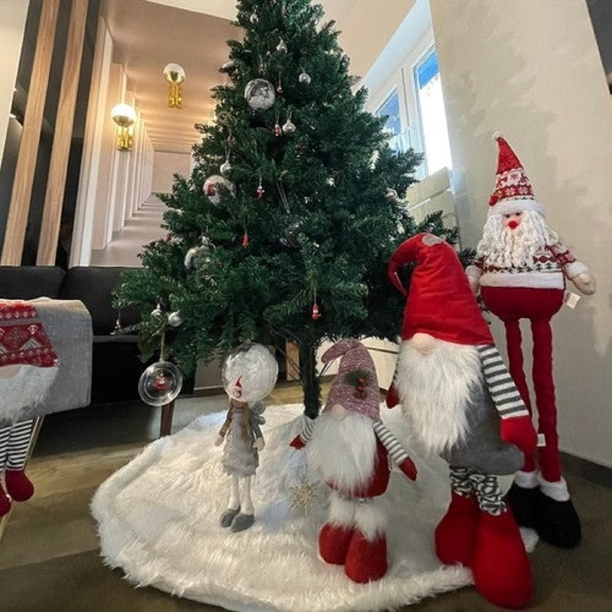 Weihnachtsbaum mit Schmuck und Wichtel- und Weihnachtsmannfiguren auf weißem Teppich.