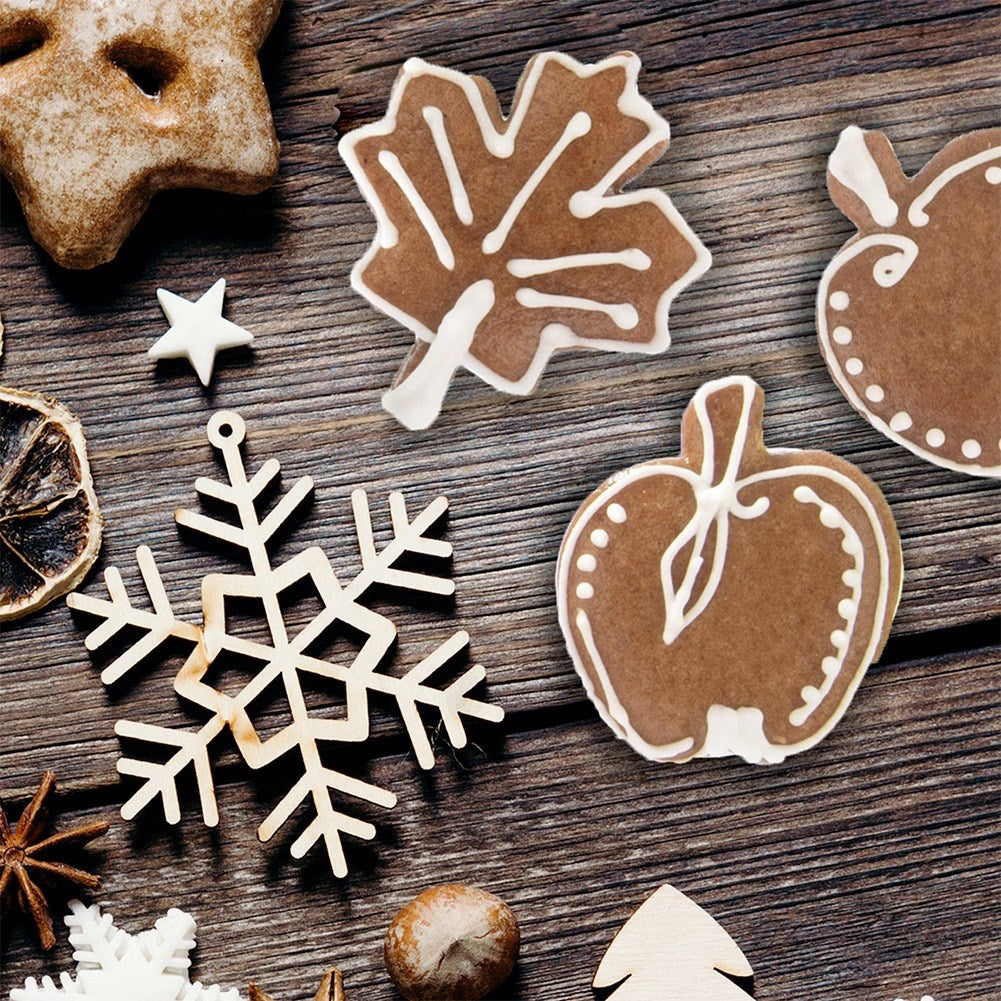 Galletas navideñas con forma de estrella, hoja, manzana y copo de nieve sobre madera.