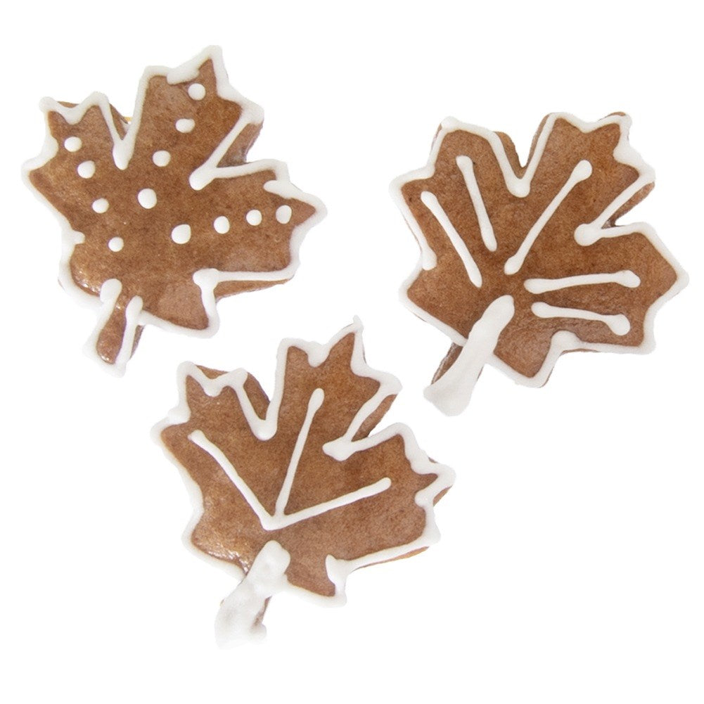 Tres galletas marrones en forma de hoja de arce decoradas con glaseado blanco.