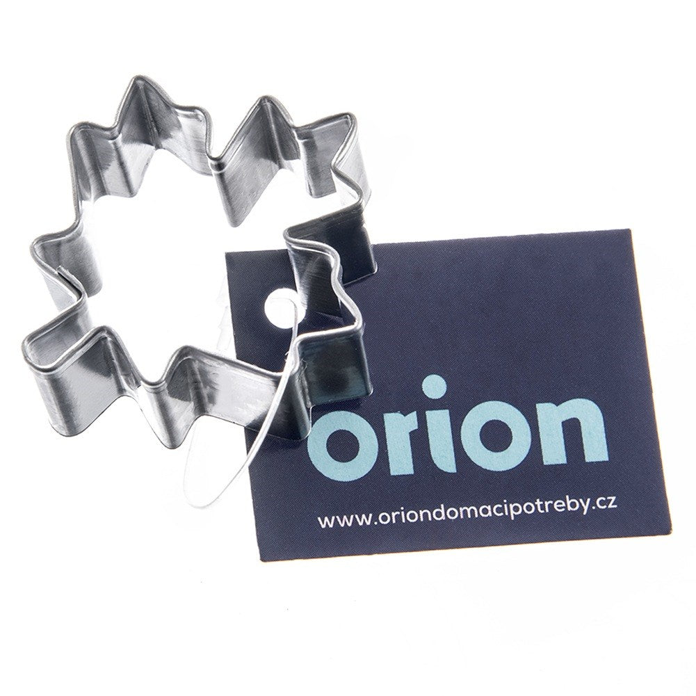 Un cortador de galletas metálico en forma de estrella junto a una tarjeta azul oscuro con Orion.