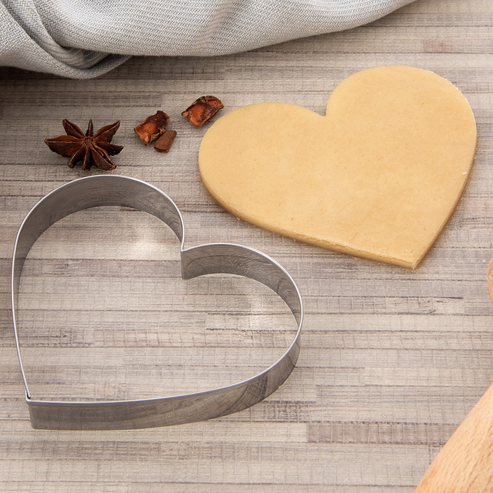 Cortador de galletas en forma de corazón y masa sobre madera con especias.