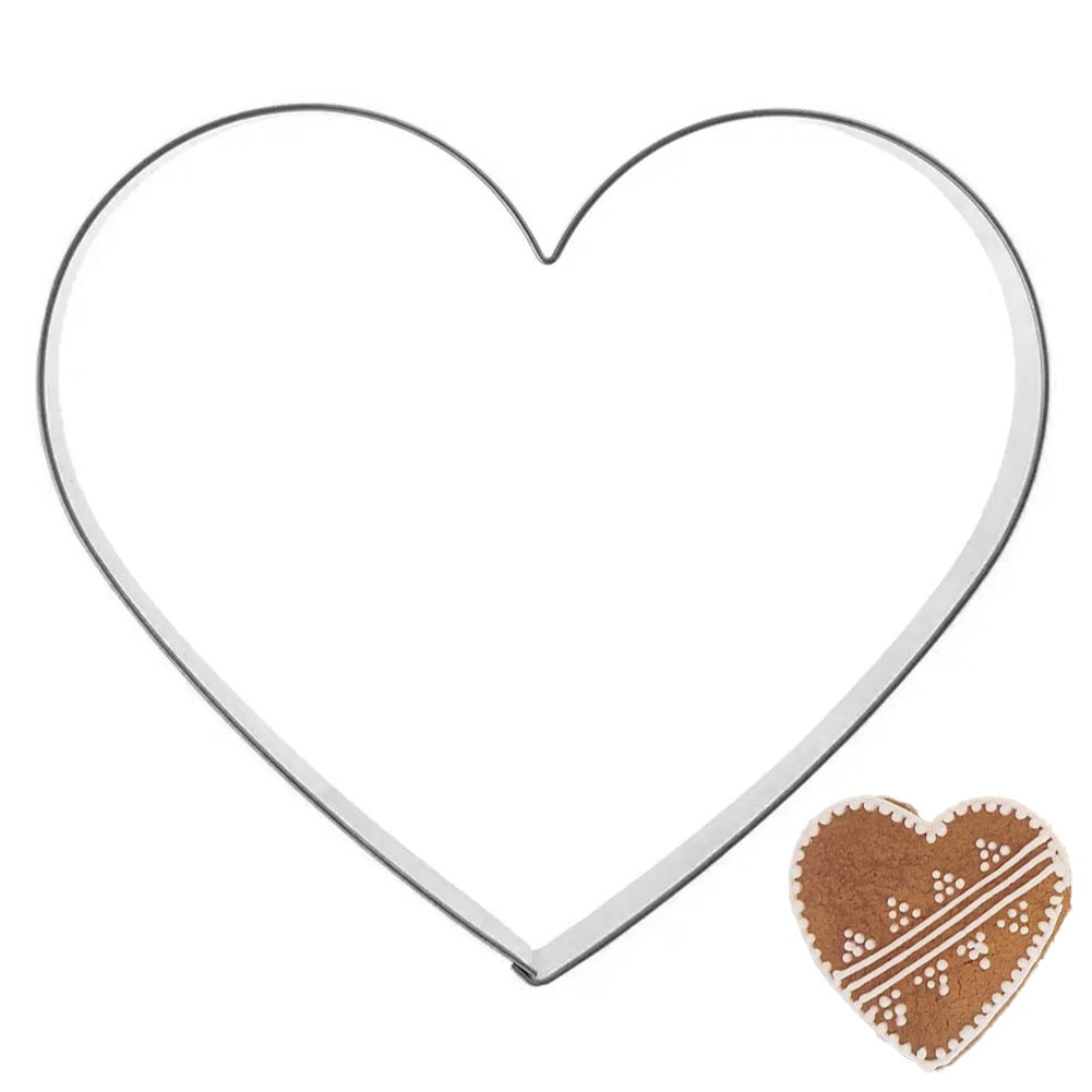 Cortador de galletas en forma de corazón junto a un pequeño corazón de jengibre decorado.