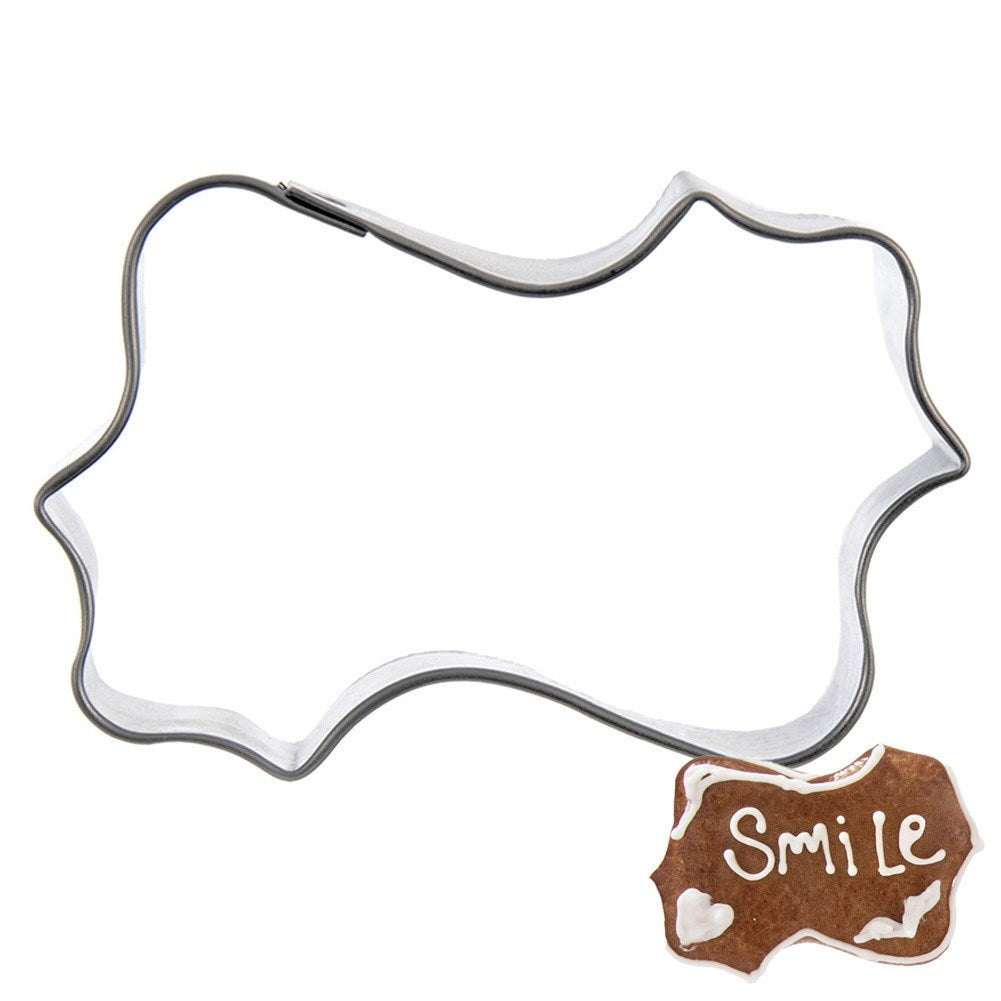 Cortador de galletas de metal en forma de bocadillo con una galleta de jengibre que dice 'Smile'.