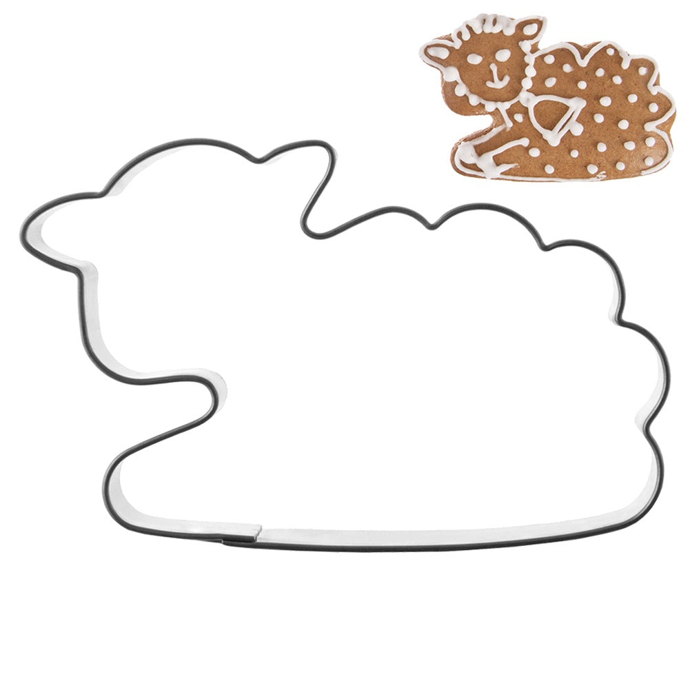 Un cordero de pan de jengibre decorado con glaseado junto a un cortador de galletas en forma de nube.