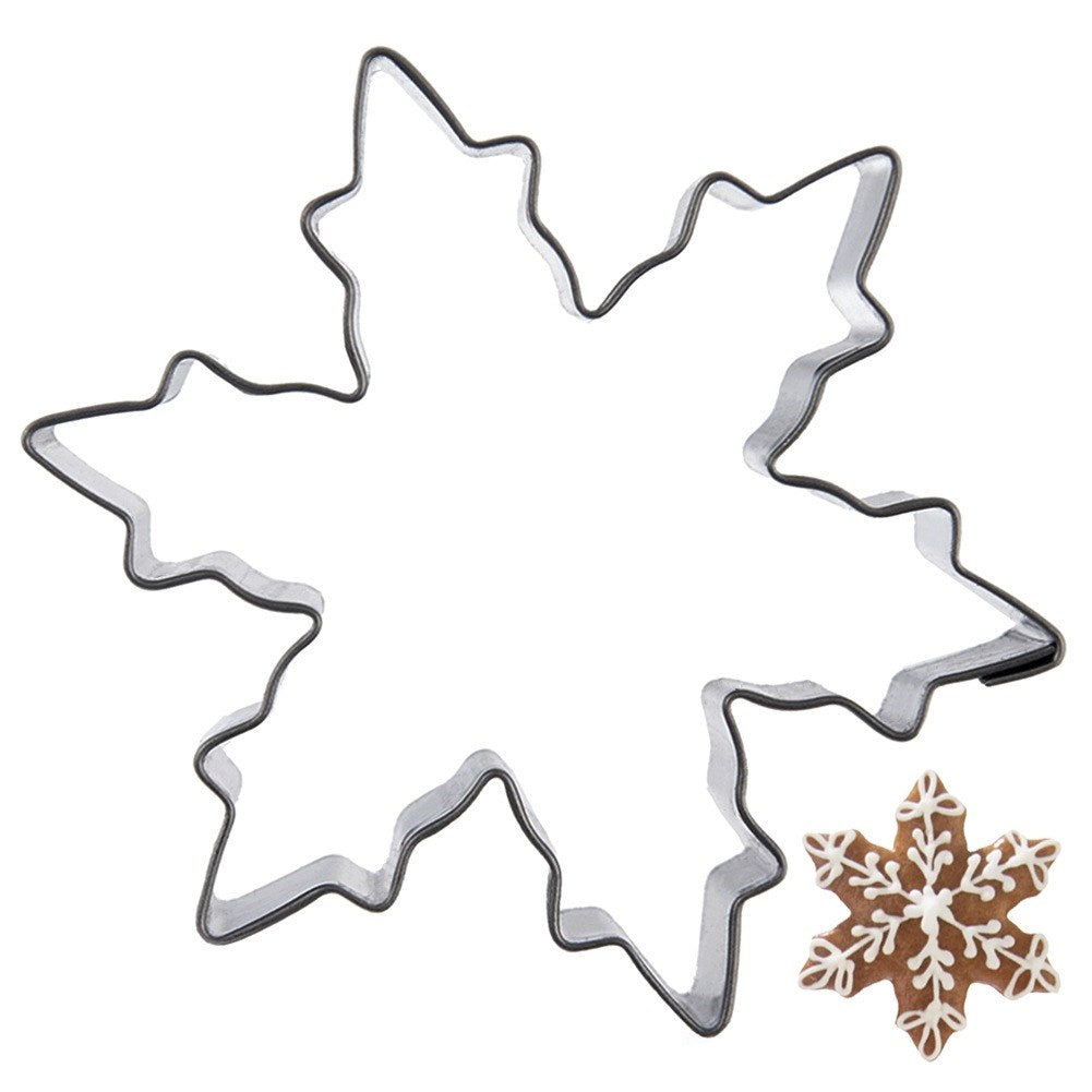 Un cortador de galletas de copo de nieve metálico junto a una galleta de copo de nieve marrón.