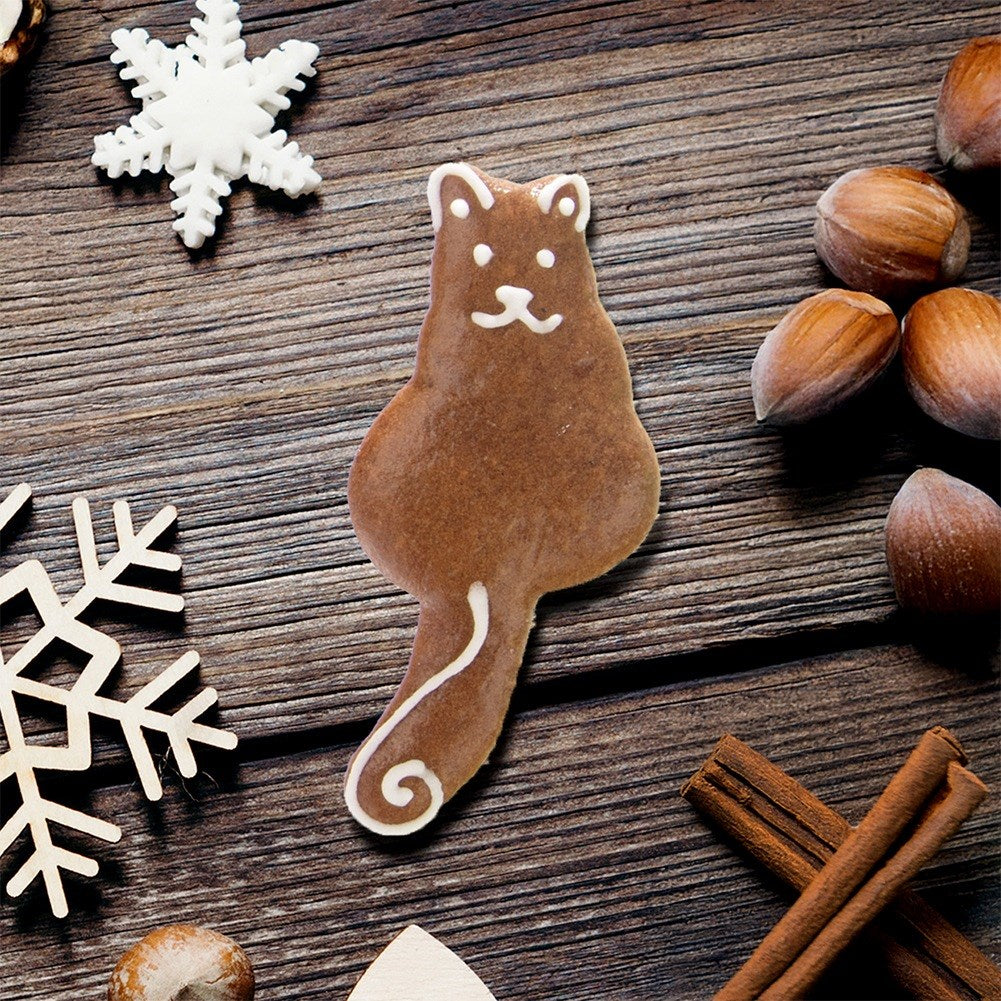 Una galleta de jengibre marrón con forma de gato y glaseado blanco sobre mesa.