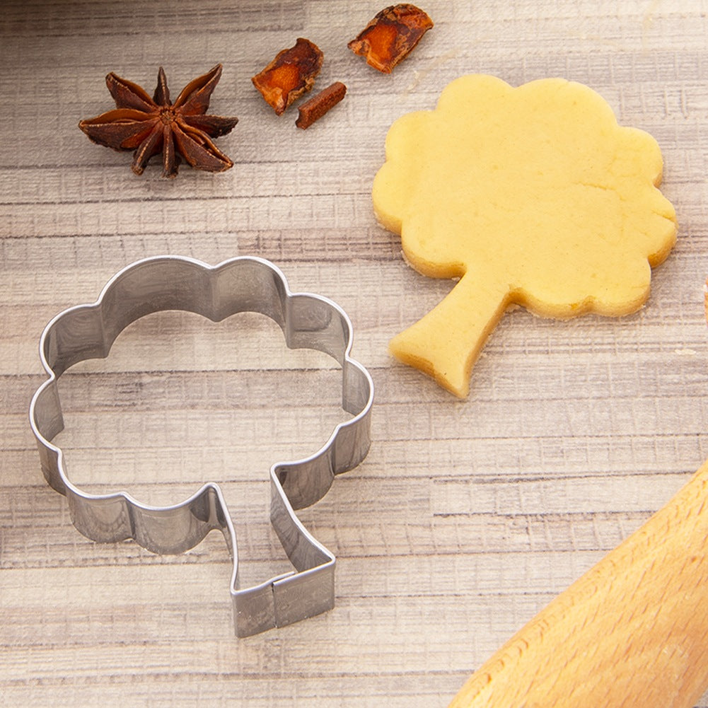 Un cortador de galletas con forma de árbol, una galleta de árbol, anís estrellado y frutos secos sobre madera.