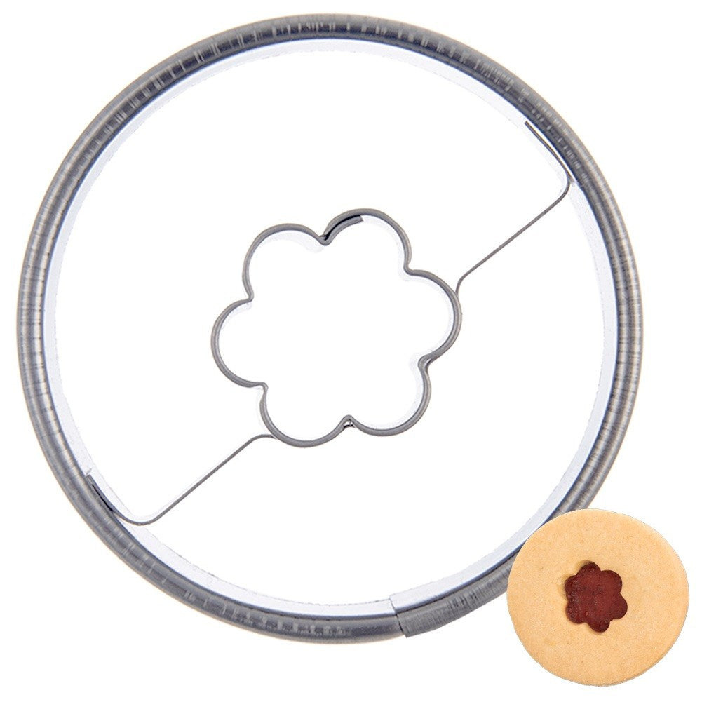 Un cortador de galletas redondo con diseño de flor y una galleta pequeña.