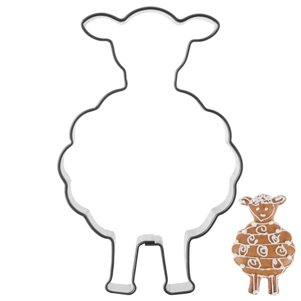 Una galleta de jengibre de oveja con glaseado blanco junto a un cortador de metal.