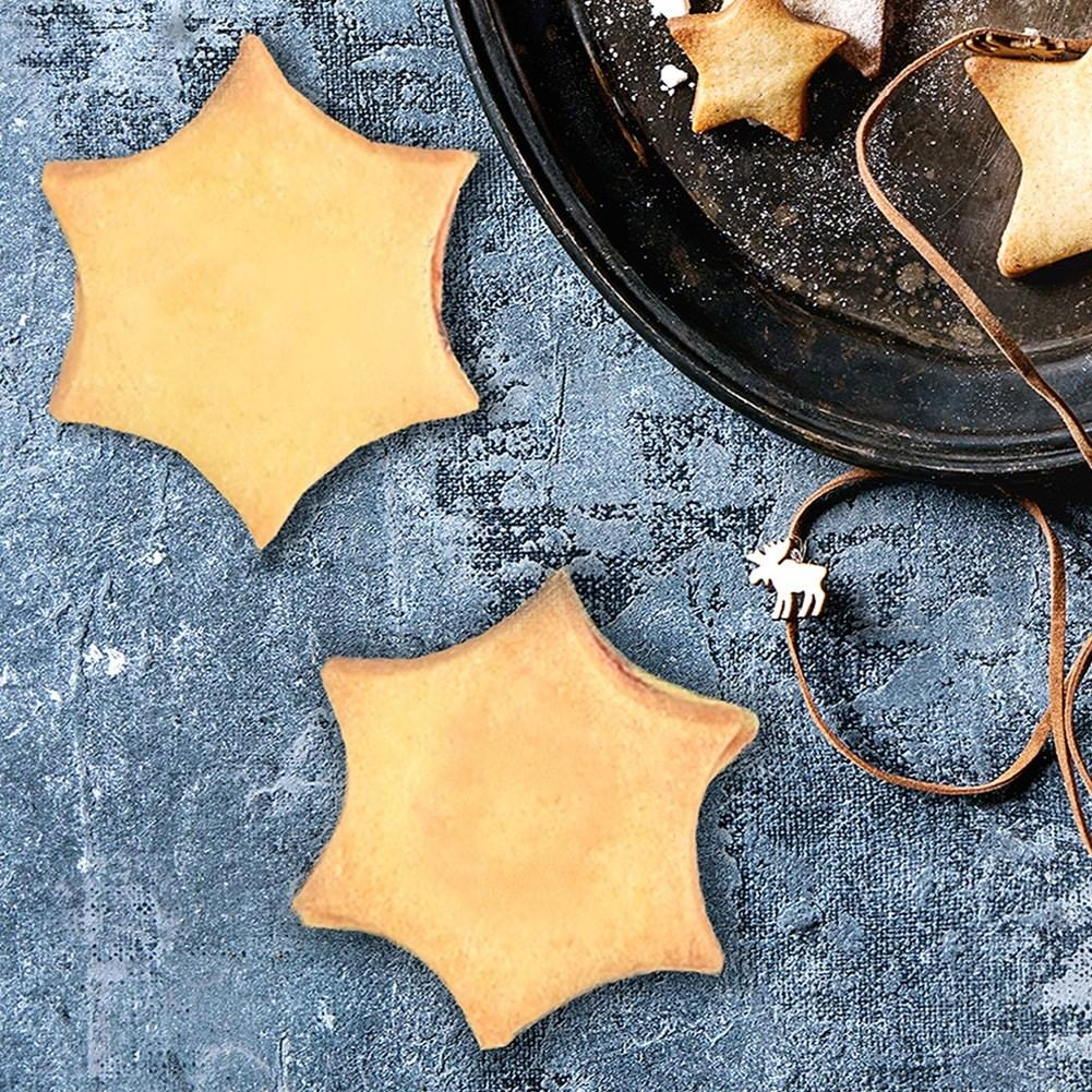 Dos galletas en forma de estrella sobre superficie azul texturizada, con más galletas en bandeja oscura.
