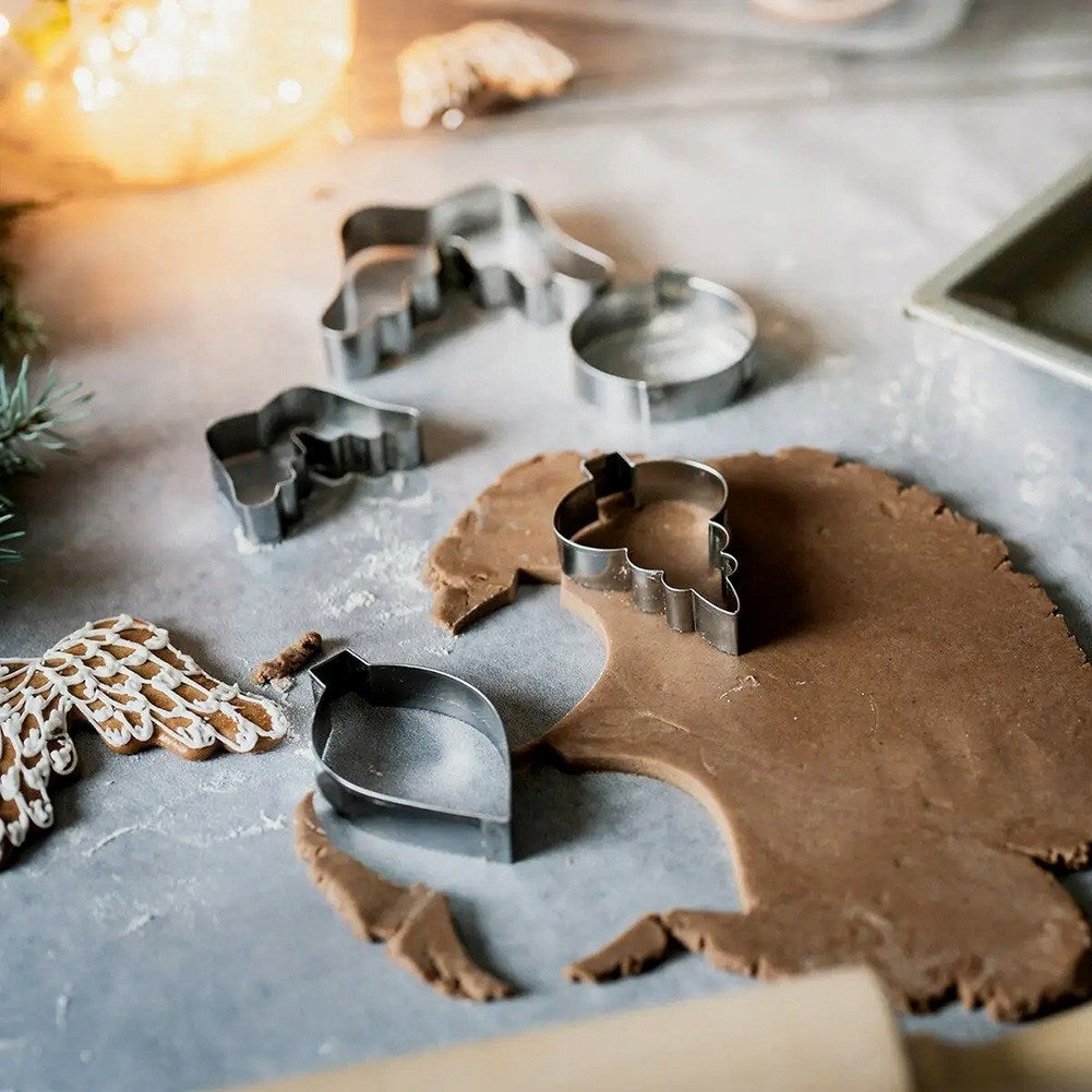 Cortadores de galletas y masa para hornear Navidad, con galletas al fondo.