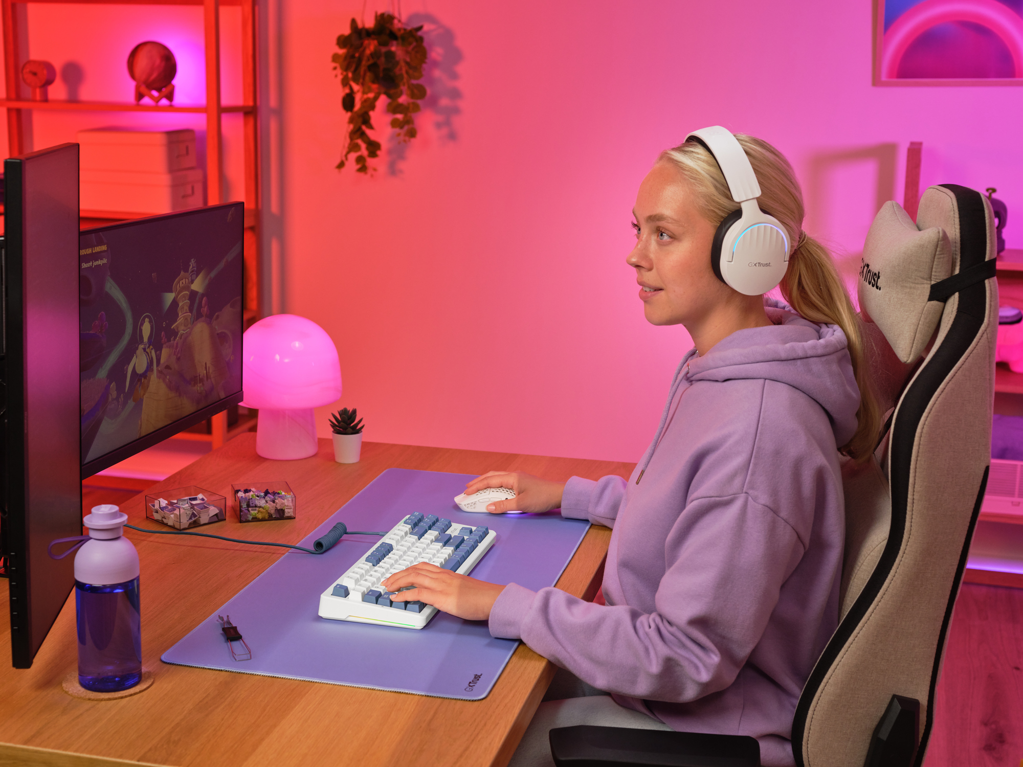 Eine Frau mit Kopfhörern spielt am Computer in einem Raum mit rosa Beleuchtung.