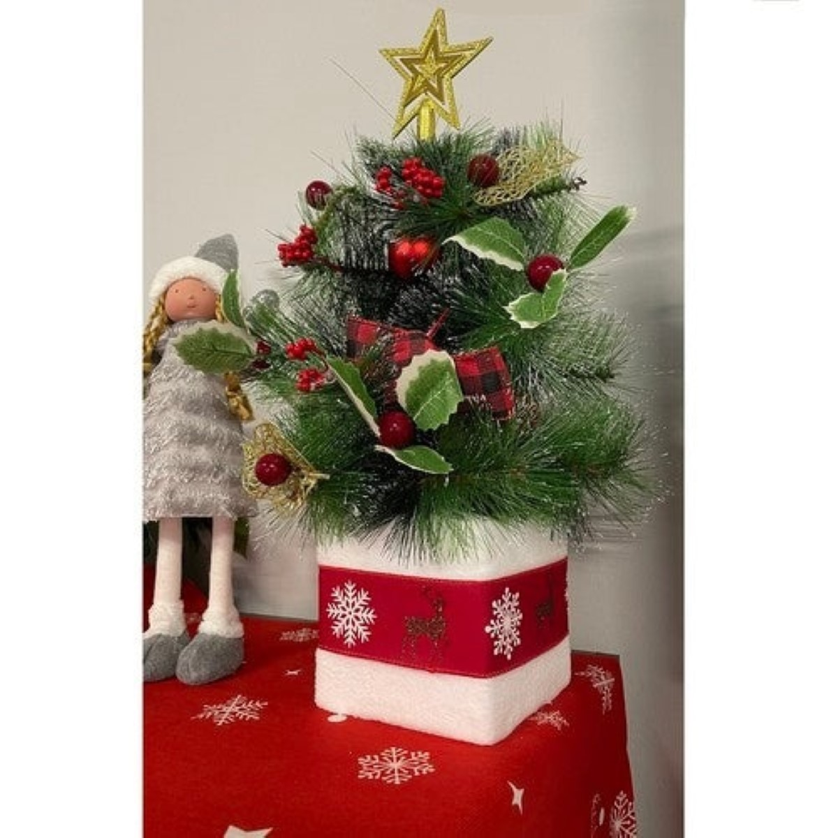 Un árbol de Navidad decorativo con estrella, bayas y una muñeca al lado.
