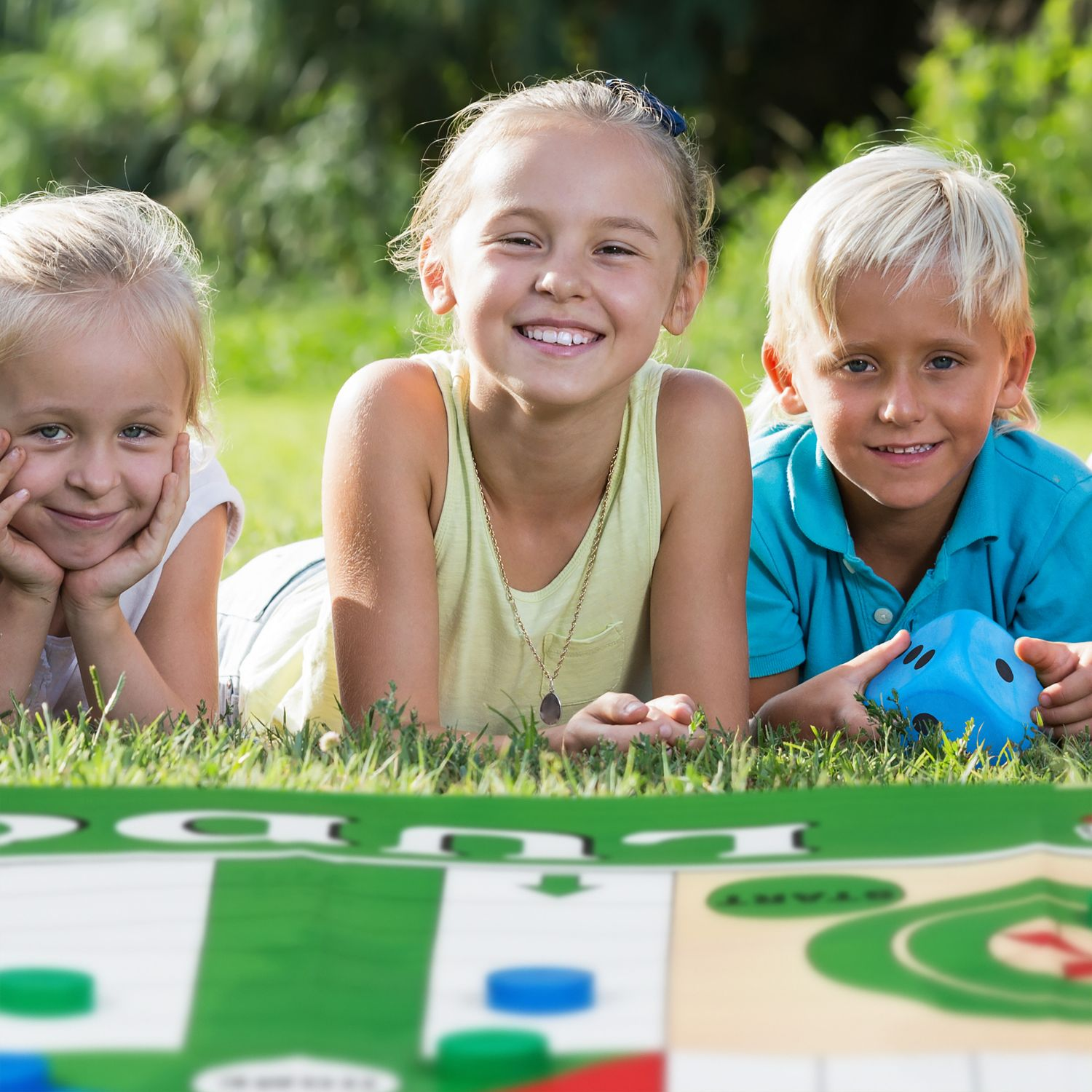 Tres niños yacen en la hierba ante un tablero de juego. Uno sostiene un dado.