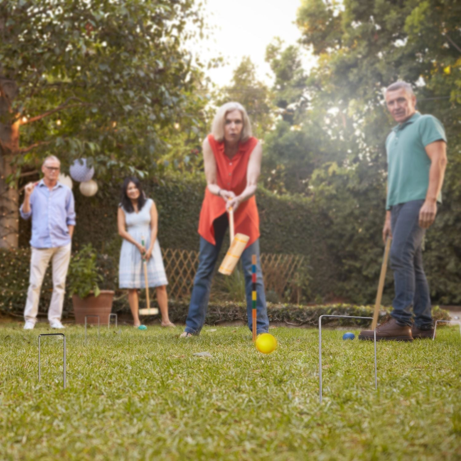 Cuatro personas juegan al croquet en un jardín al atardecer.