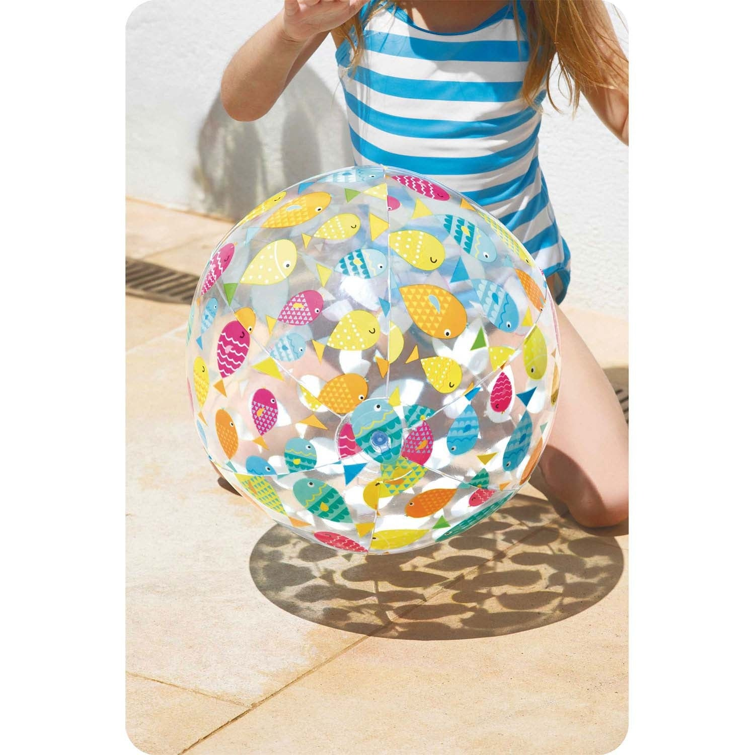 Una niña con traje de baño a rayas sostiene una pelota transparente con peces de colores.