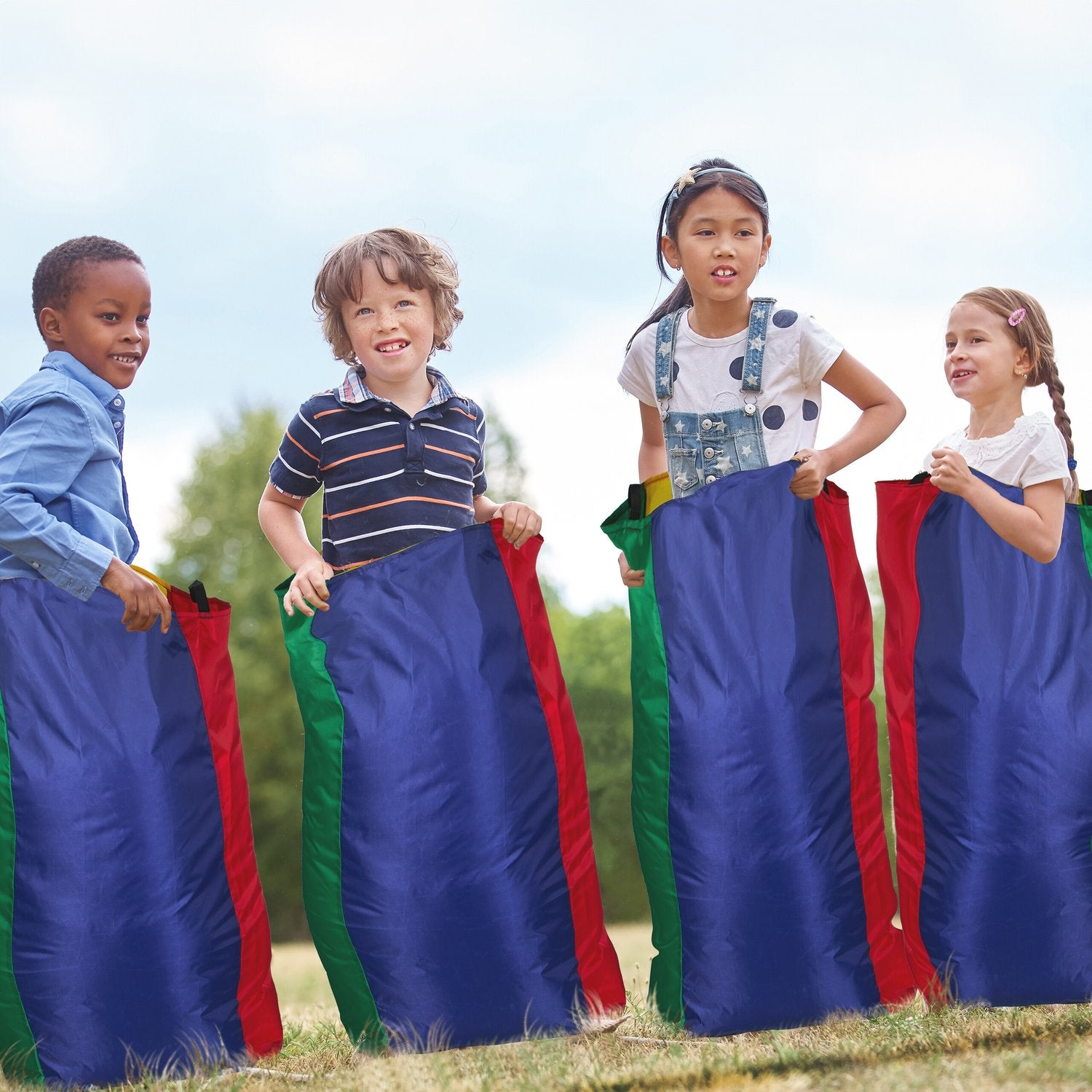 Cuatro niños en sacos para carreras de sacos al aire libre, sacos azules, rojos y verdes.