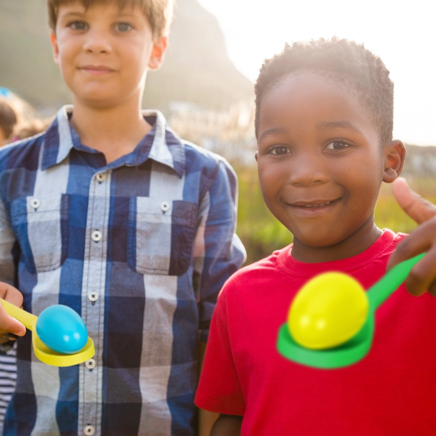 Dos niños sostienen cucharas con huevos. Uno viste de rojo, el otro de azul.