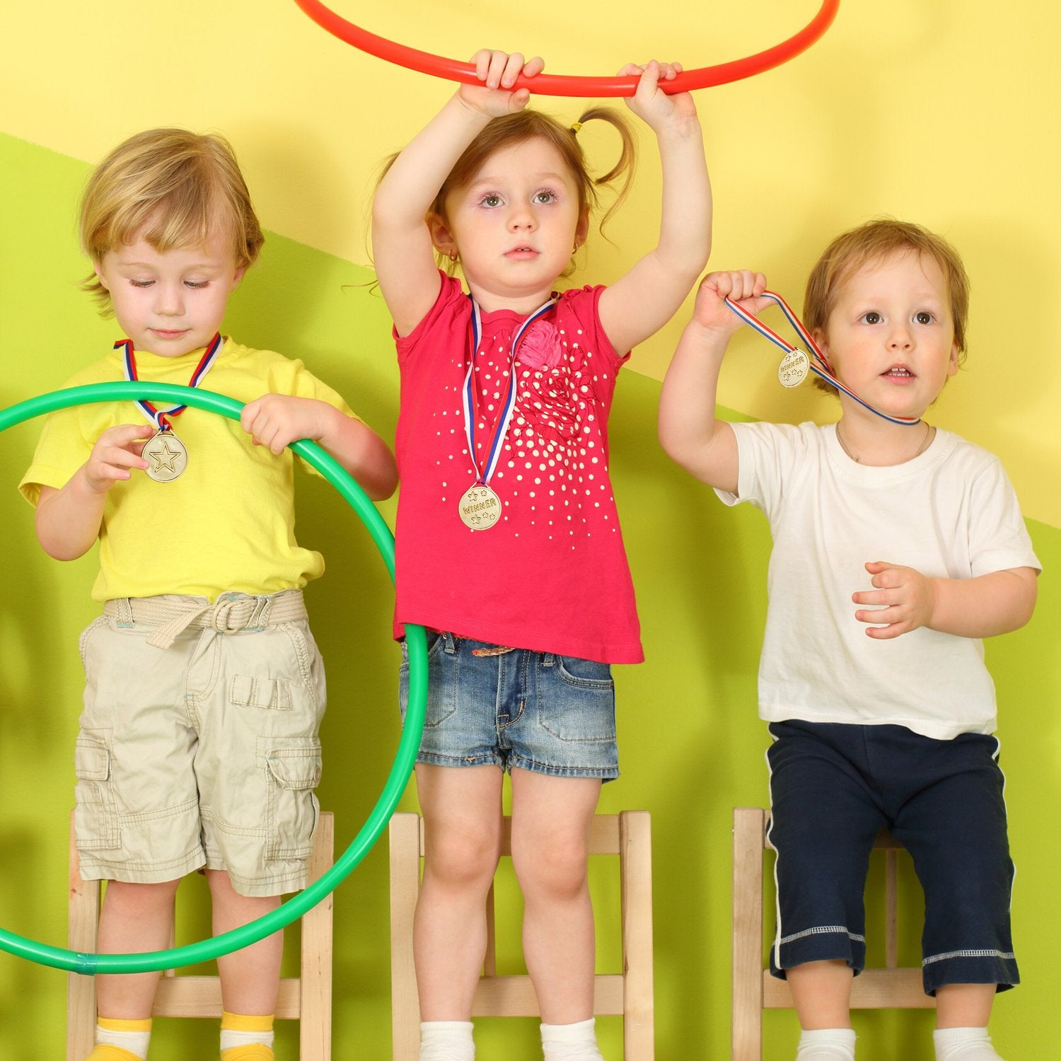 Tres niños con aros y medallas se paran en sillas.