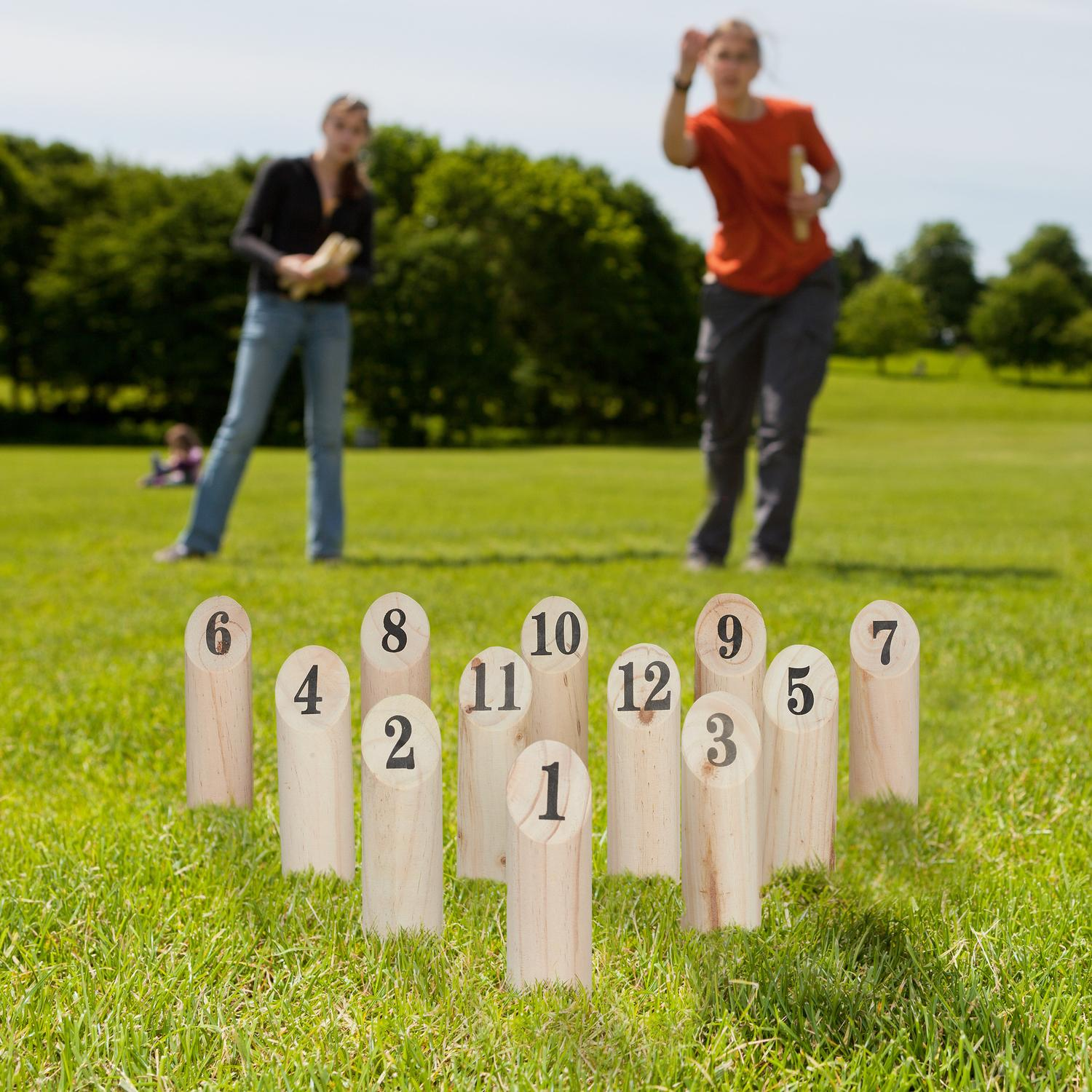 Bolos de madera con números en un campo de césped, dos personas juegan al fondo.