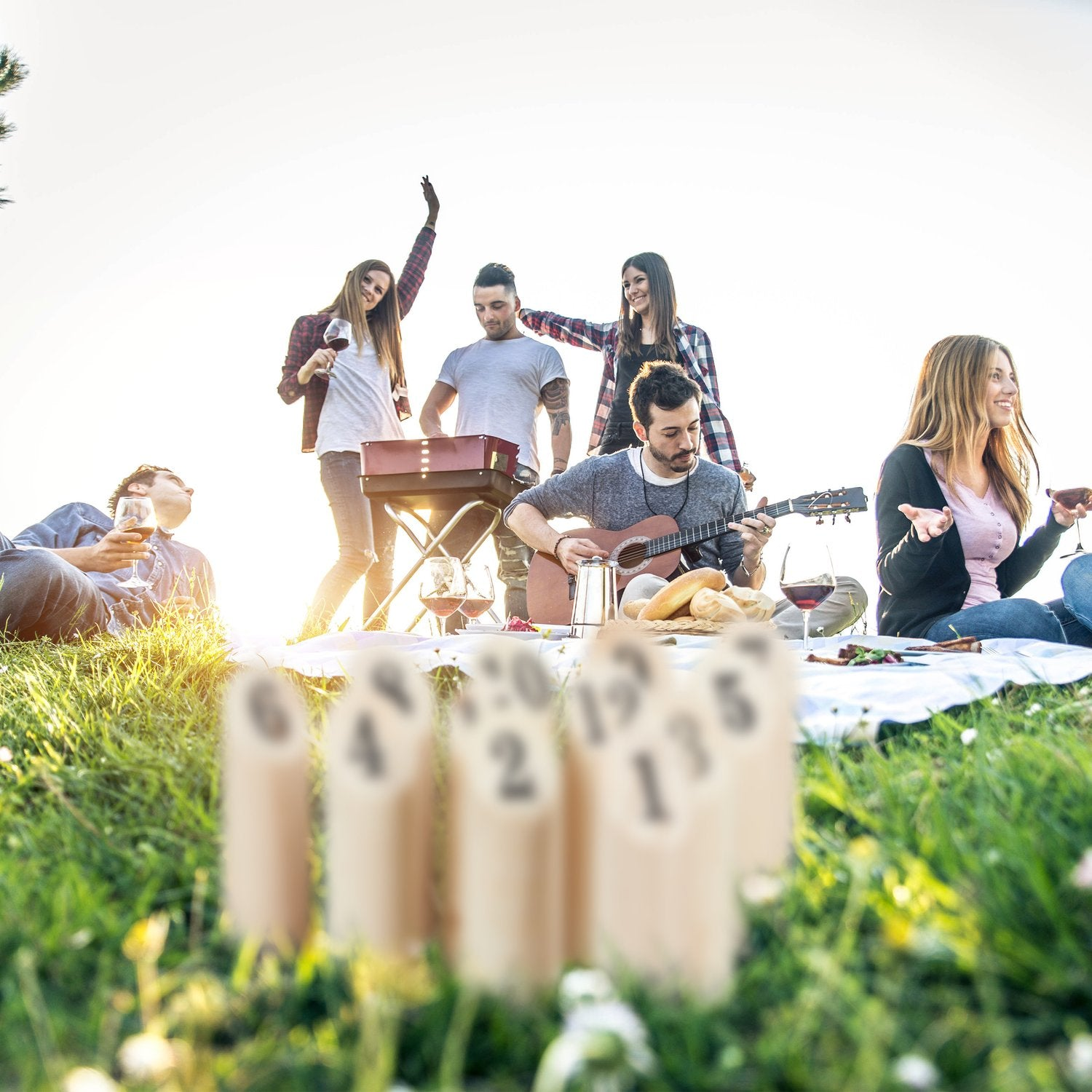 Amigos disfrutan un picnic al aire libre, tocando la guitarra y asando comida.