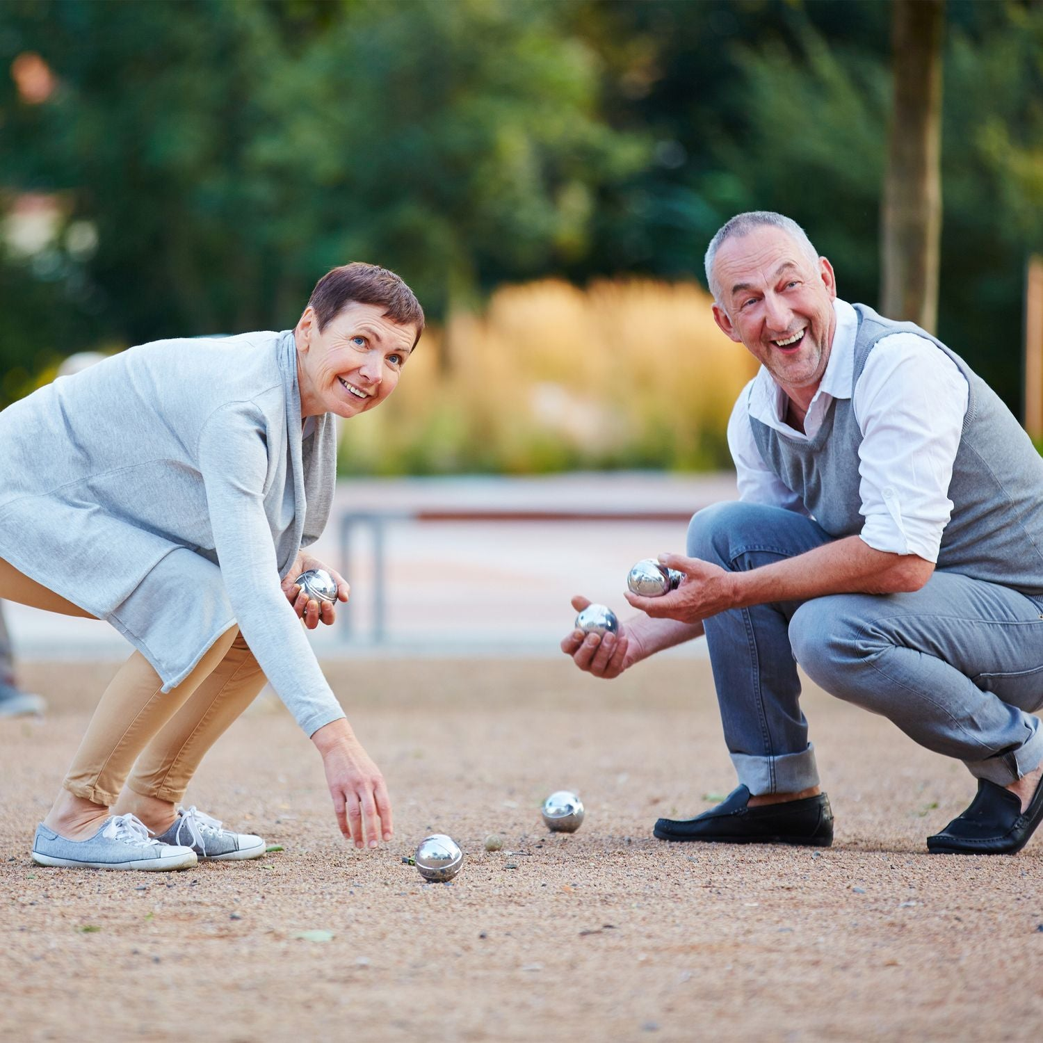 Pareja de ancianos jugando a la petanca al aire libre, ambos sonríen y sostienen bolas de metal.