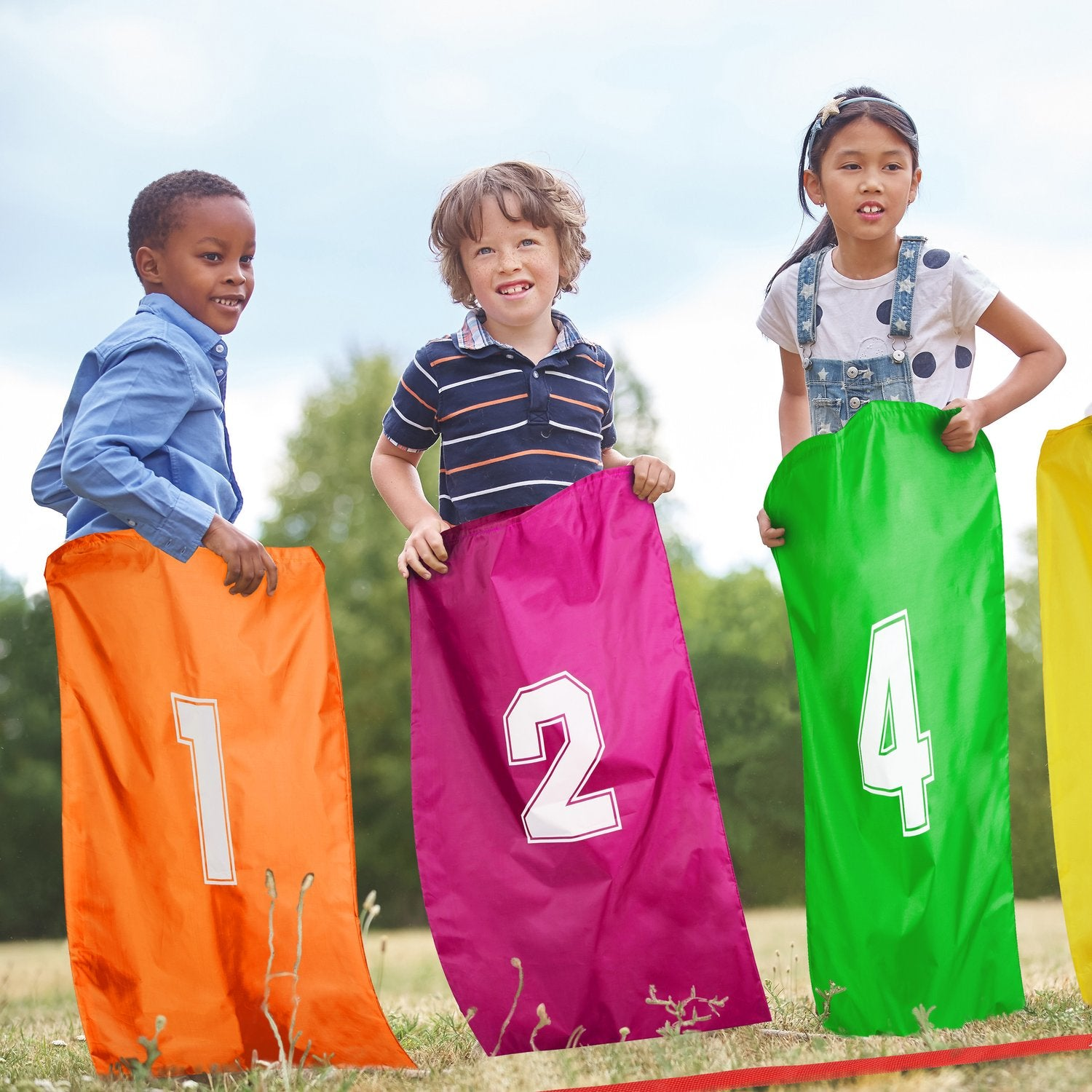 Tres niños afuera sosteniendo sacos numerados, listos para una carrera.