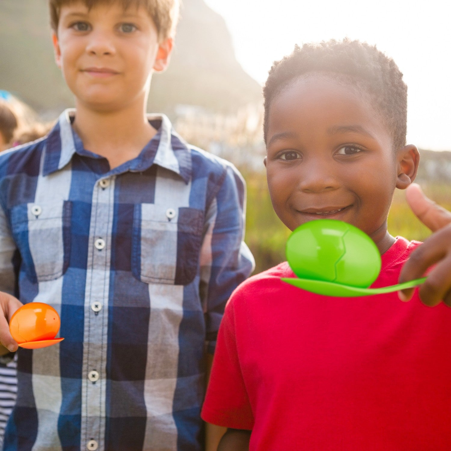 Dos niños compiten con huevos en cucharas. Uno sostiene un huevo naranja, el otro uno verde.