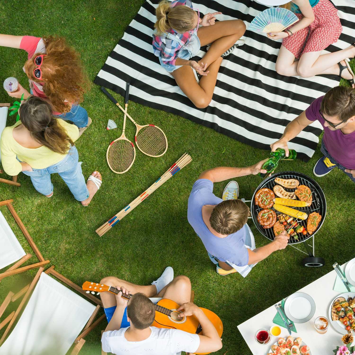 Gente haciendo una barbacoa y jugando en el jardín. Un hombre toca la guitarra.