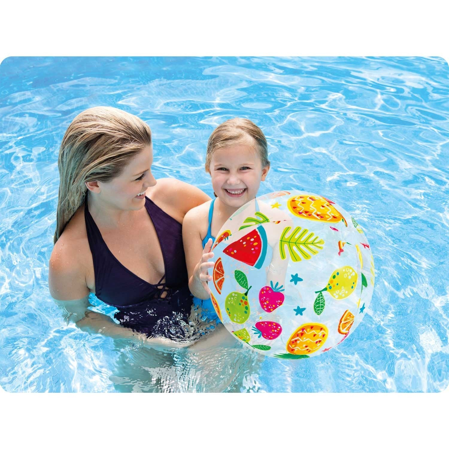 Mujer y niña en piscina con pelota de playa frutal. Agua azul brillante.