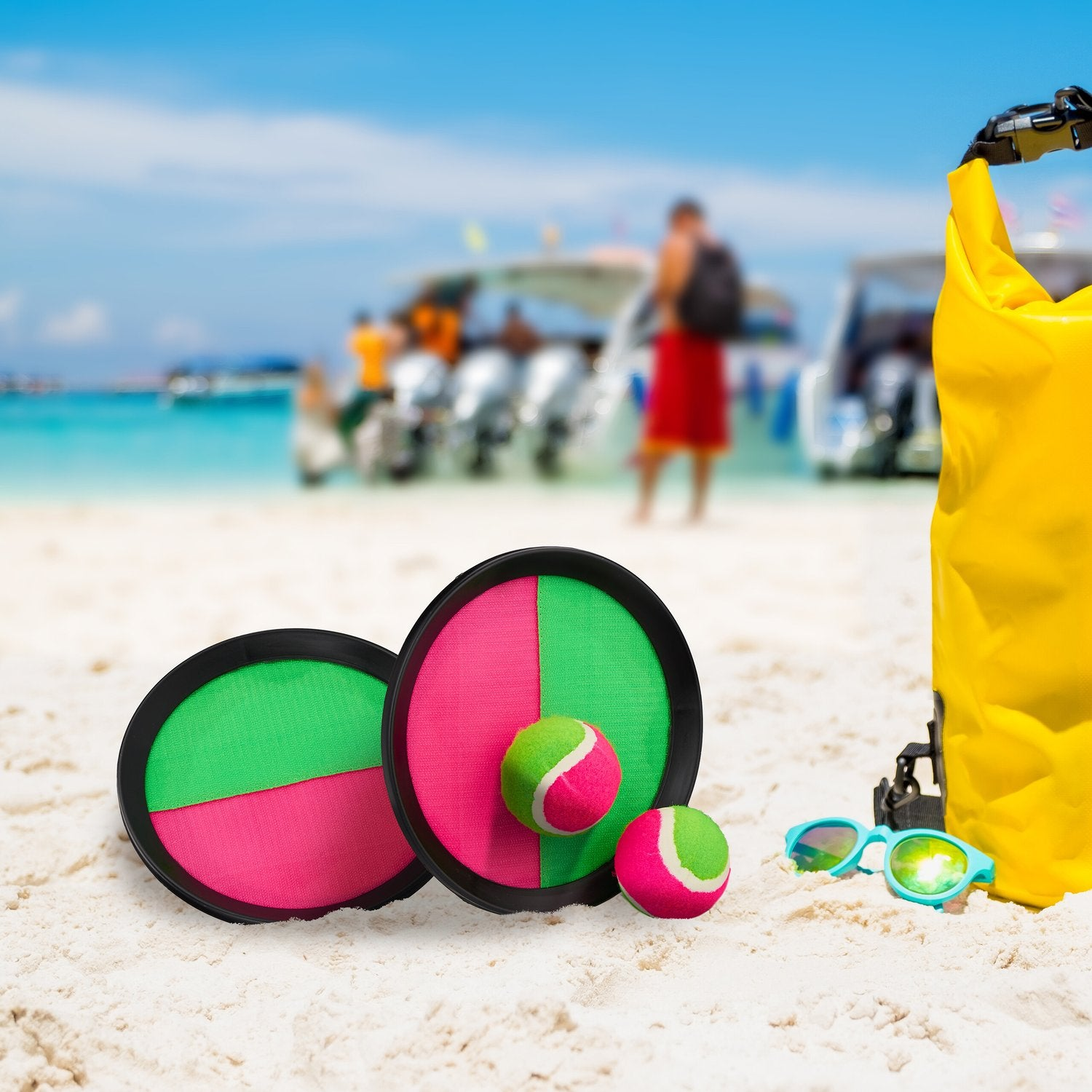 Juguetes de playa: pelotas, gafas de sol y bolsa amarilla sobre arena, mar de fondo.