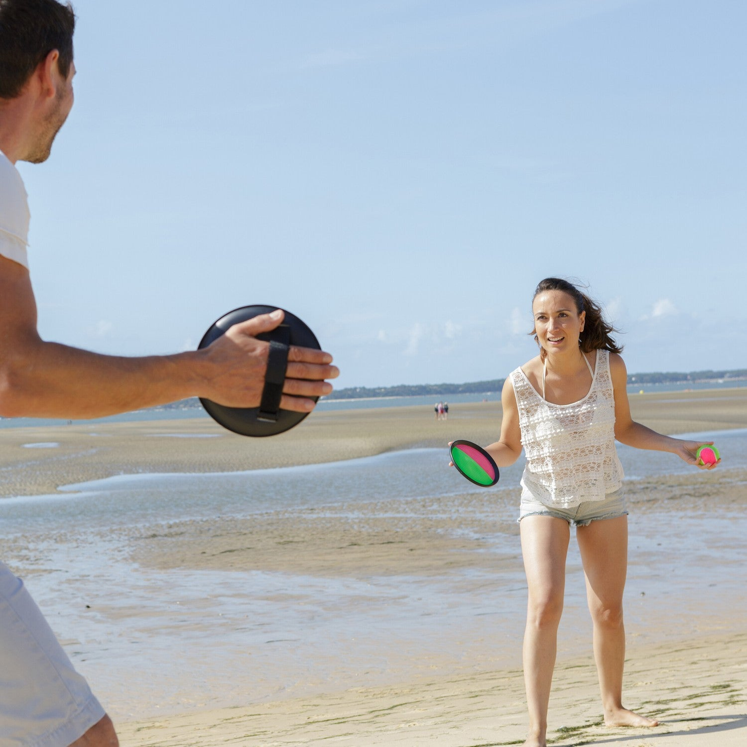 Un hombre y una mujer jugando a la pelota en la playa con marea baja.