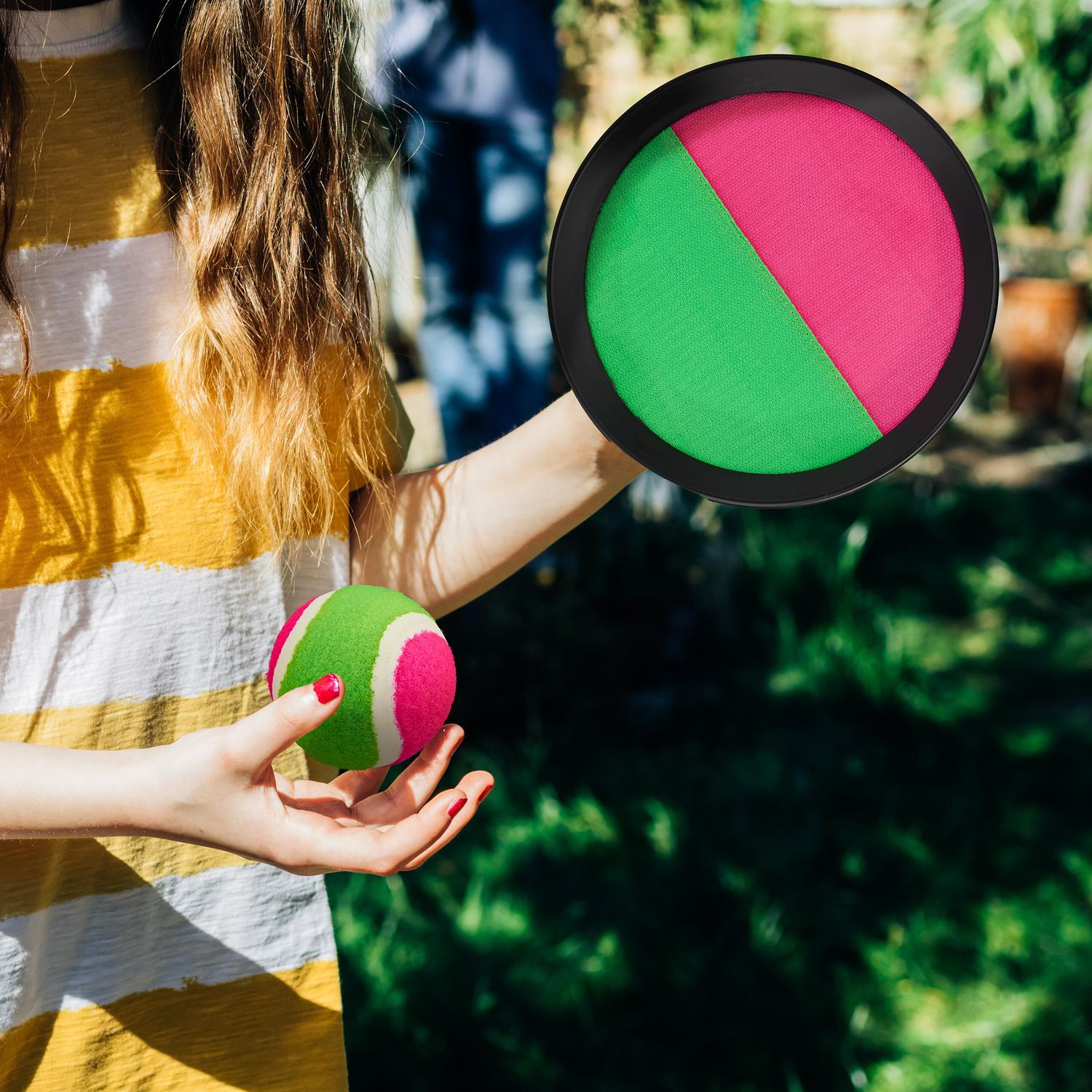 Persona sujetando una pelota con rayas rosas, verdes y blancas y un disco con campos rosas y verdes.