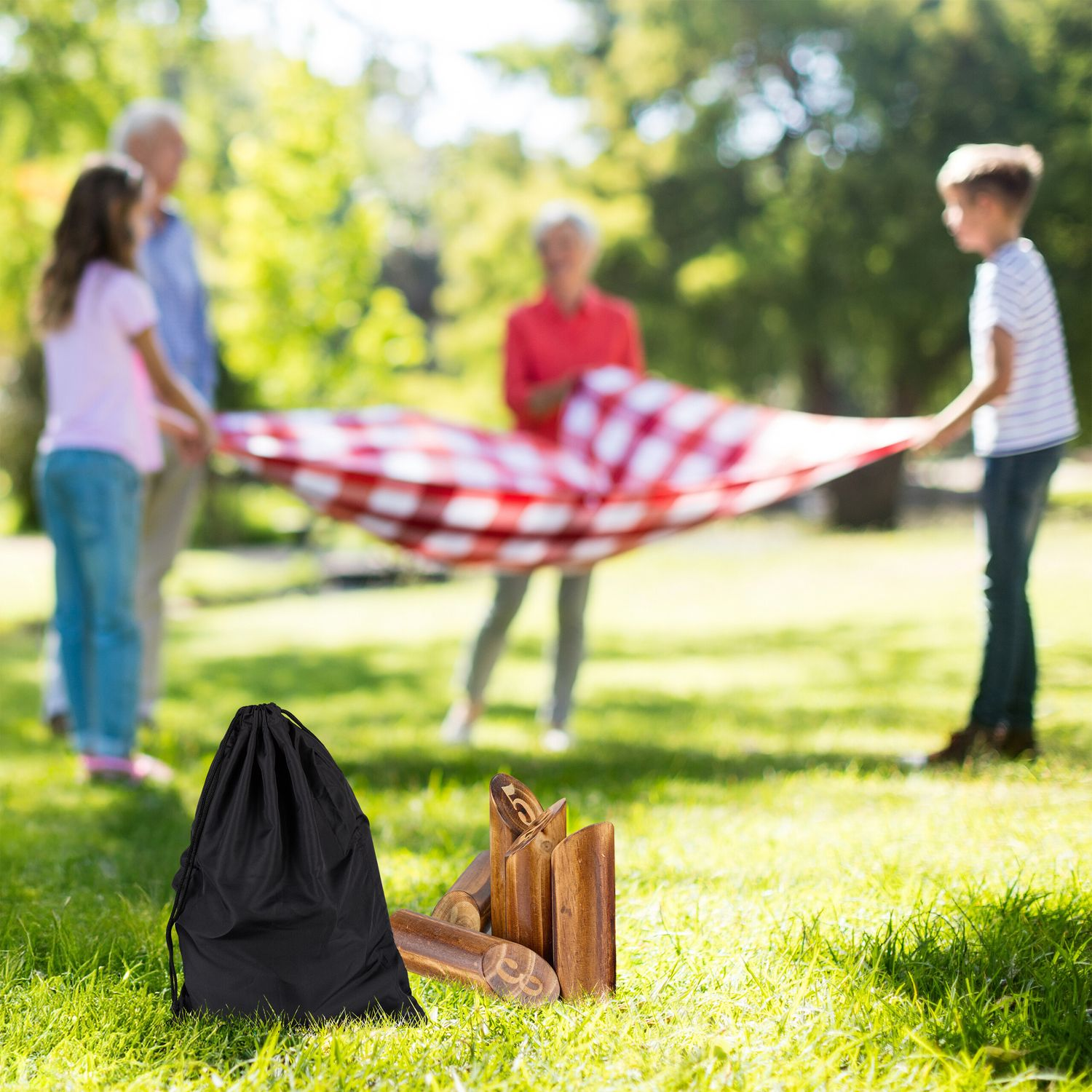Familia extiende manta de picnic, juguetes en primer plano sobre césped.