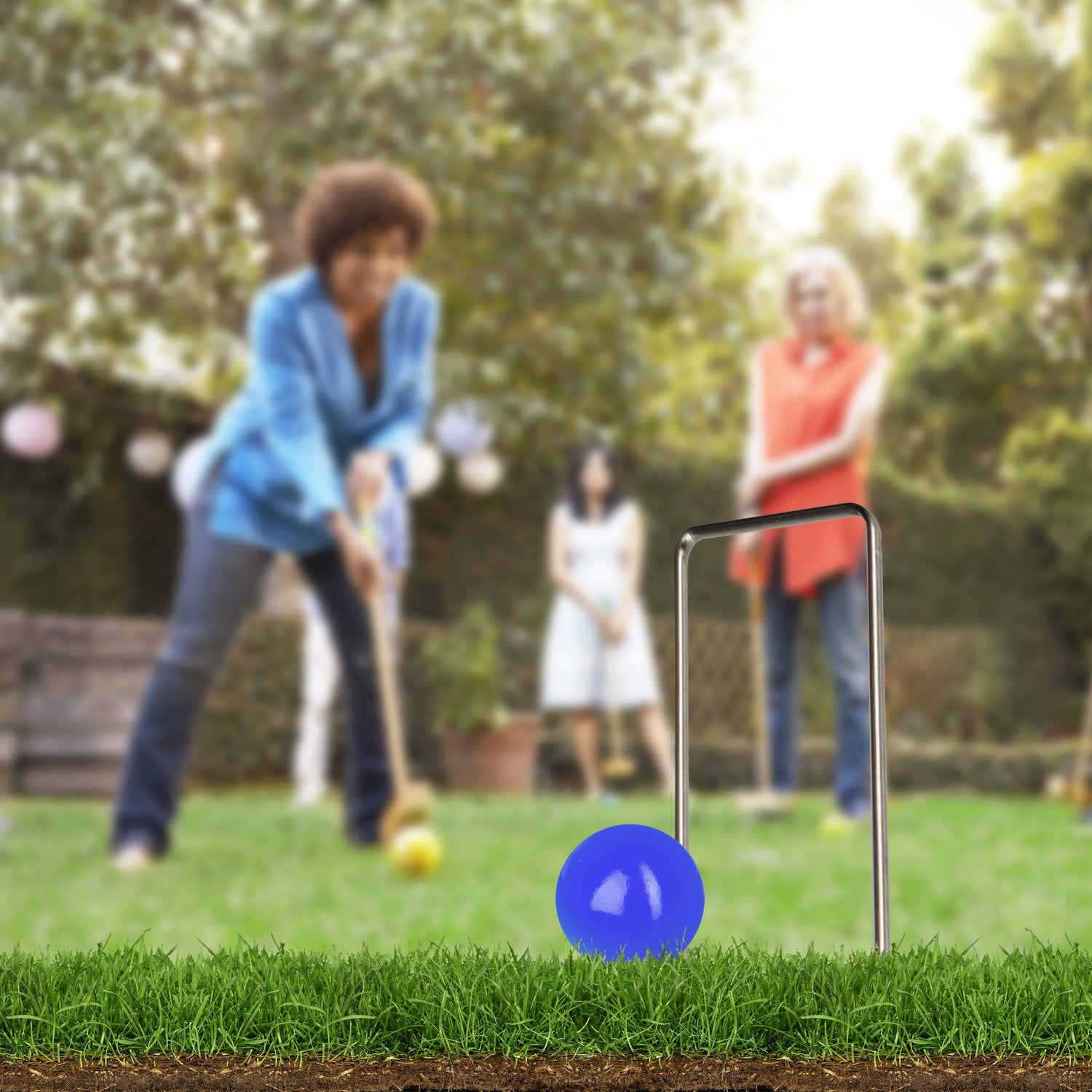 Un grupo juega al croquet en un jardín, una bola azul en primer plano.