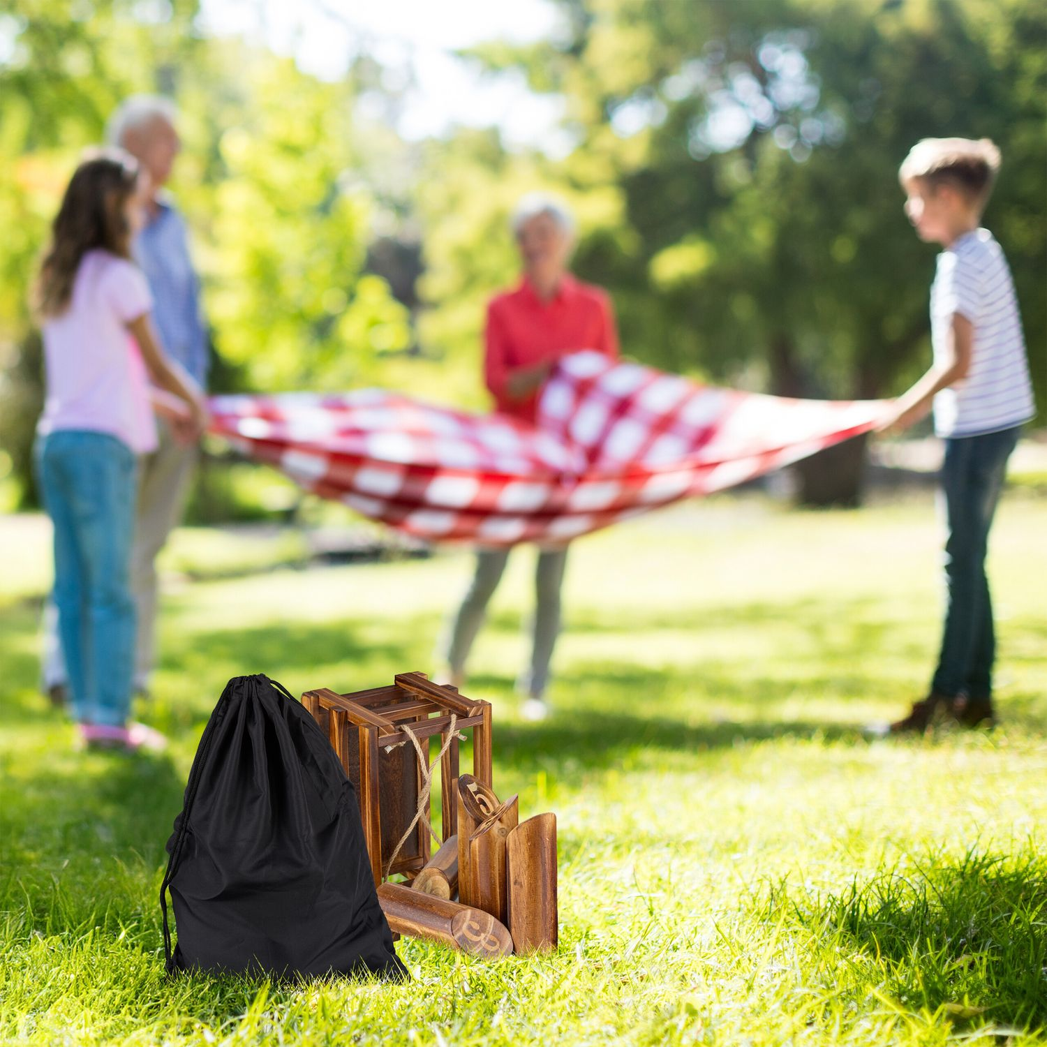 Una familia extiende una manta de picnic en el parque. En primer plano hay juguetes y una bolsa negra.
