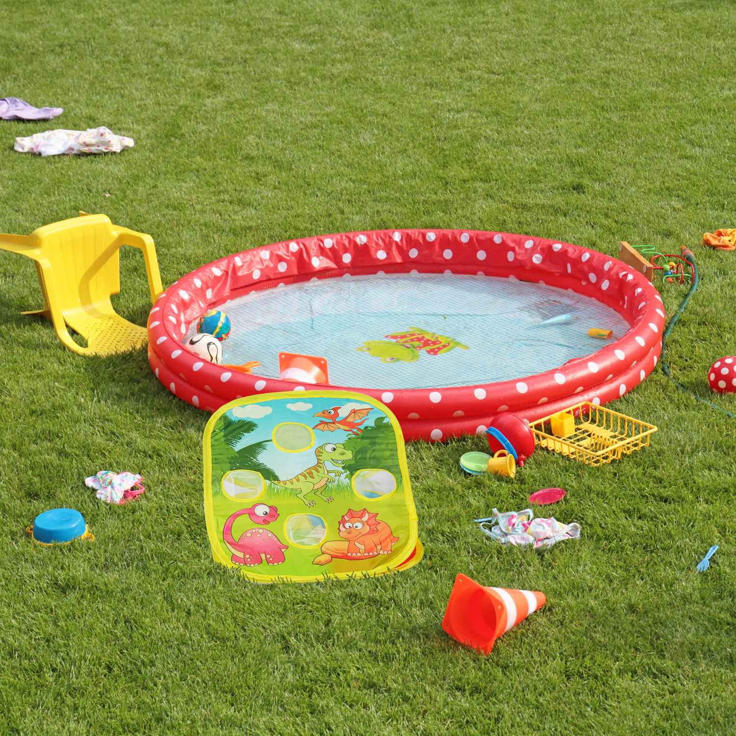 Una piscina inflable con puntos rojos se asienta sobre un césped verde. Juguetes esparcidos.